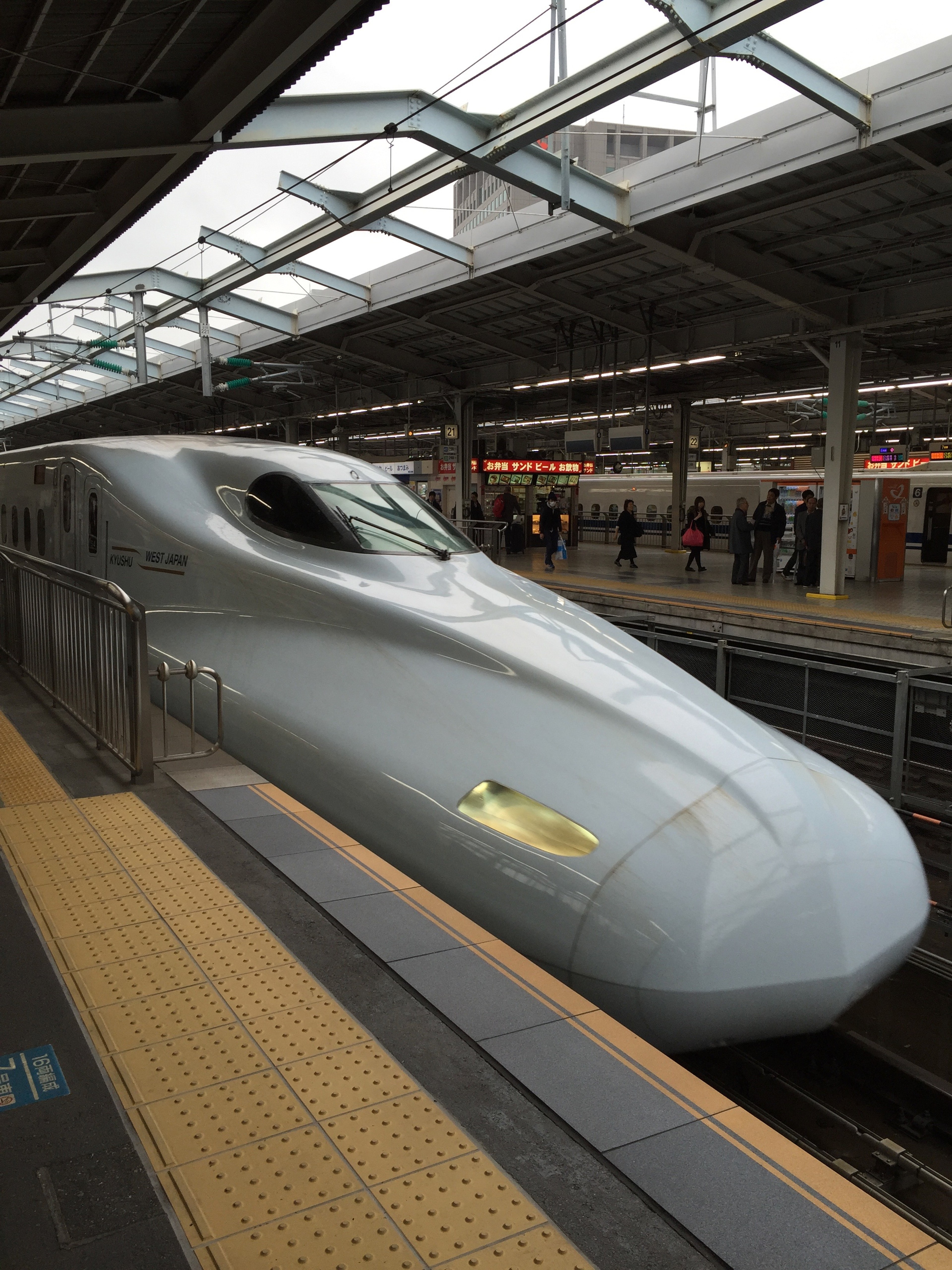 A white Shinkansen train waits at an indoor station platform.