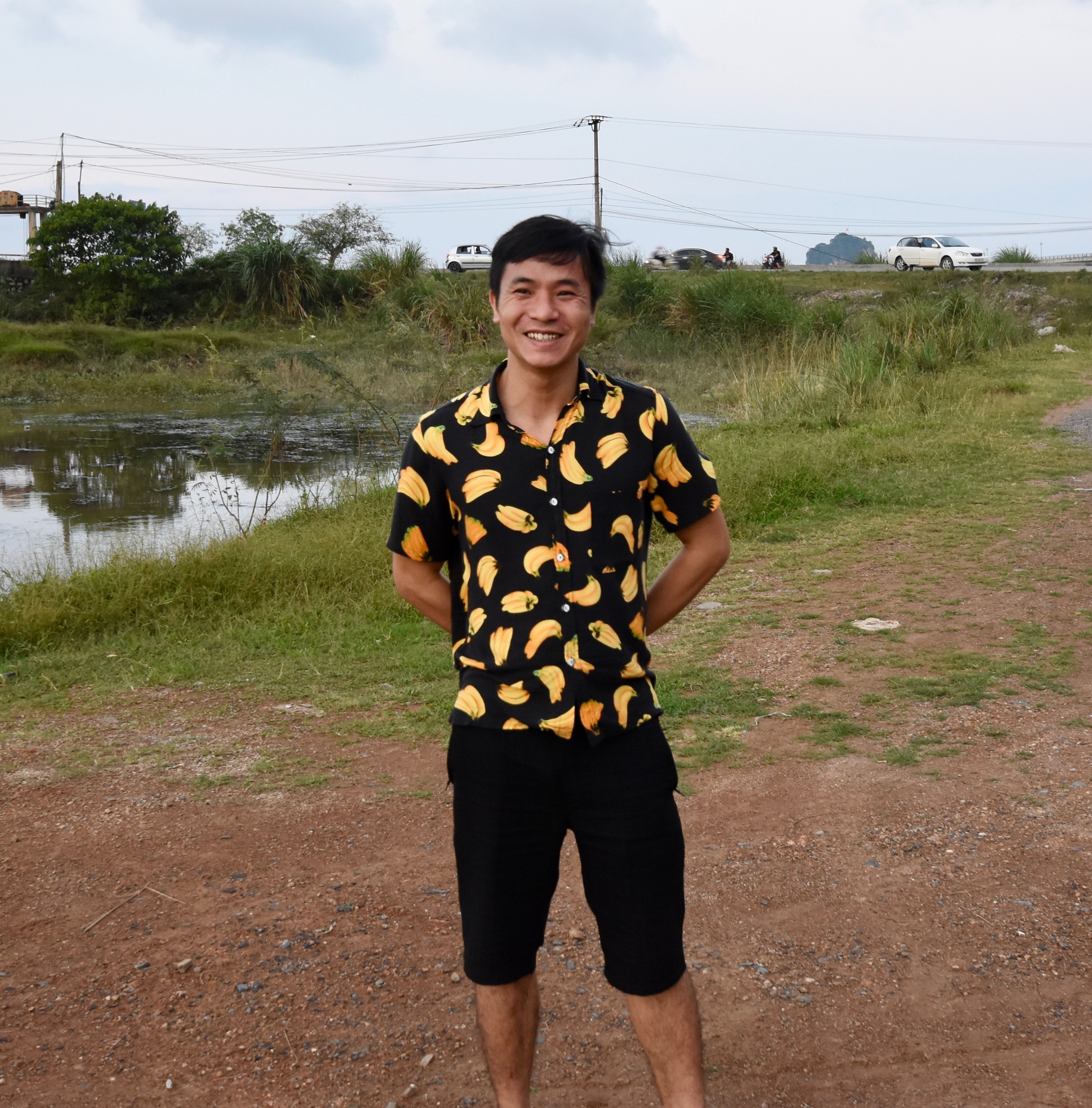 A man in a black shirt patterned with yellow shapes stands on a grassy field.