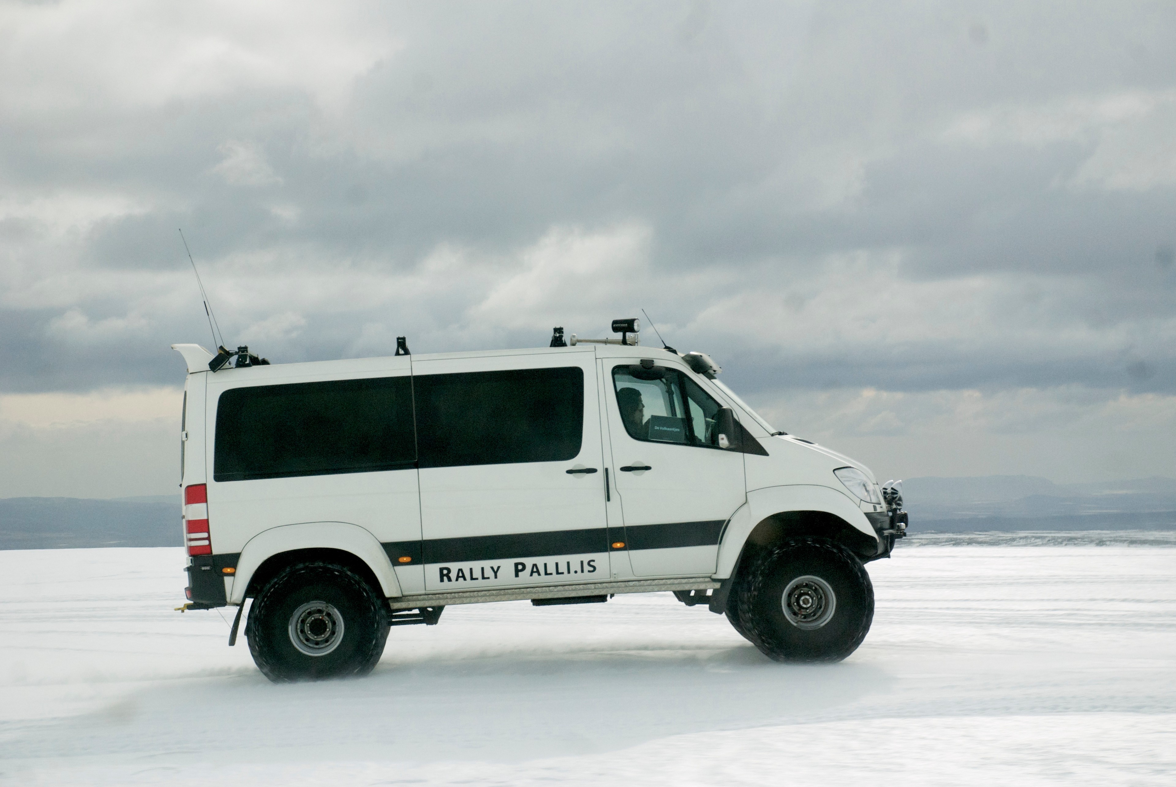 A white Super Jeep sits on an icy landscape beneath a cloudy sky.