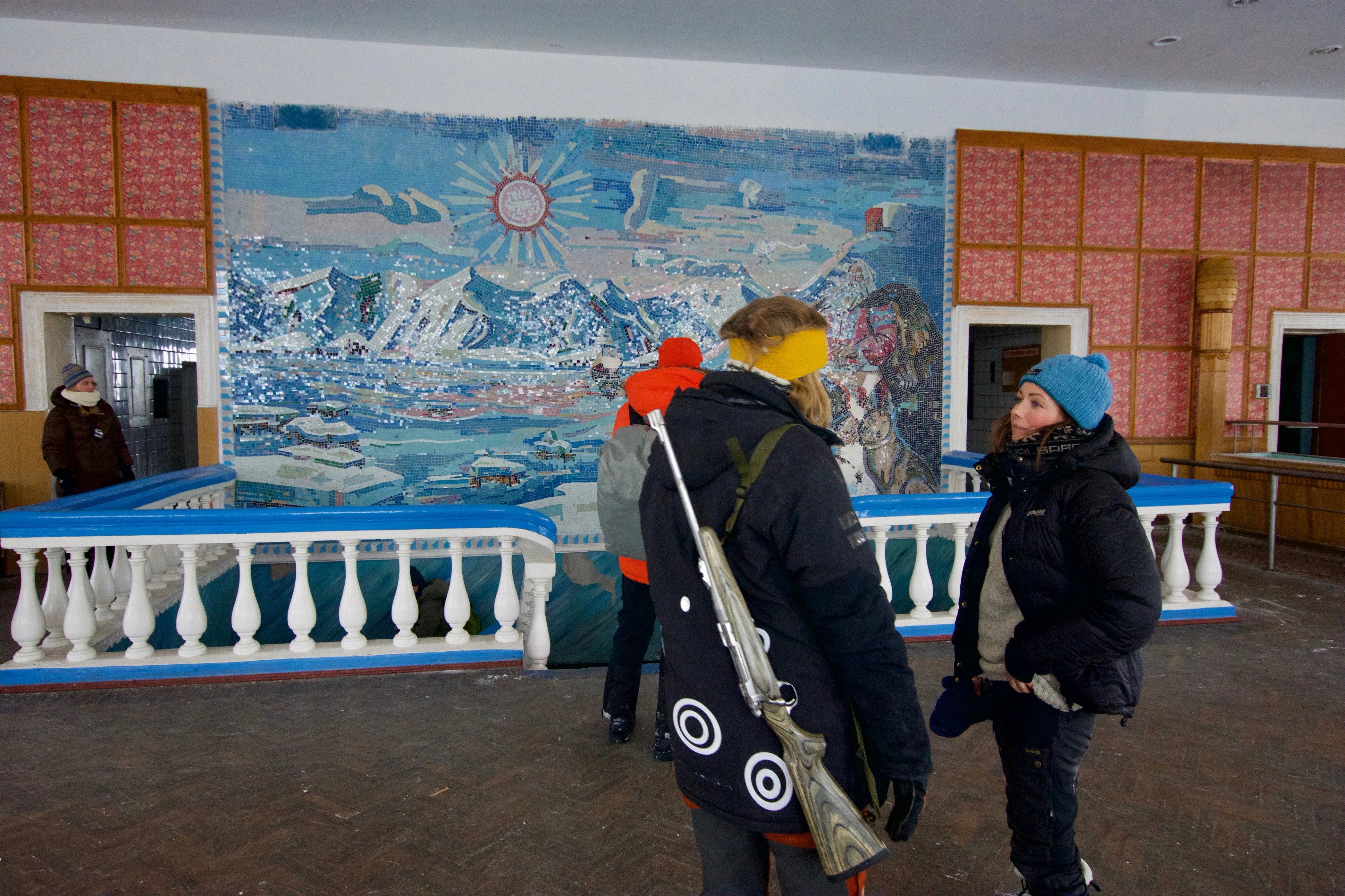 Visitors stand before a colorful wall mural in an indoor hall.