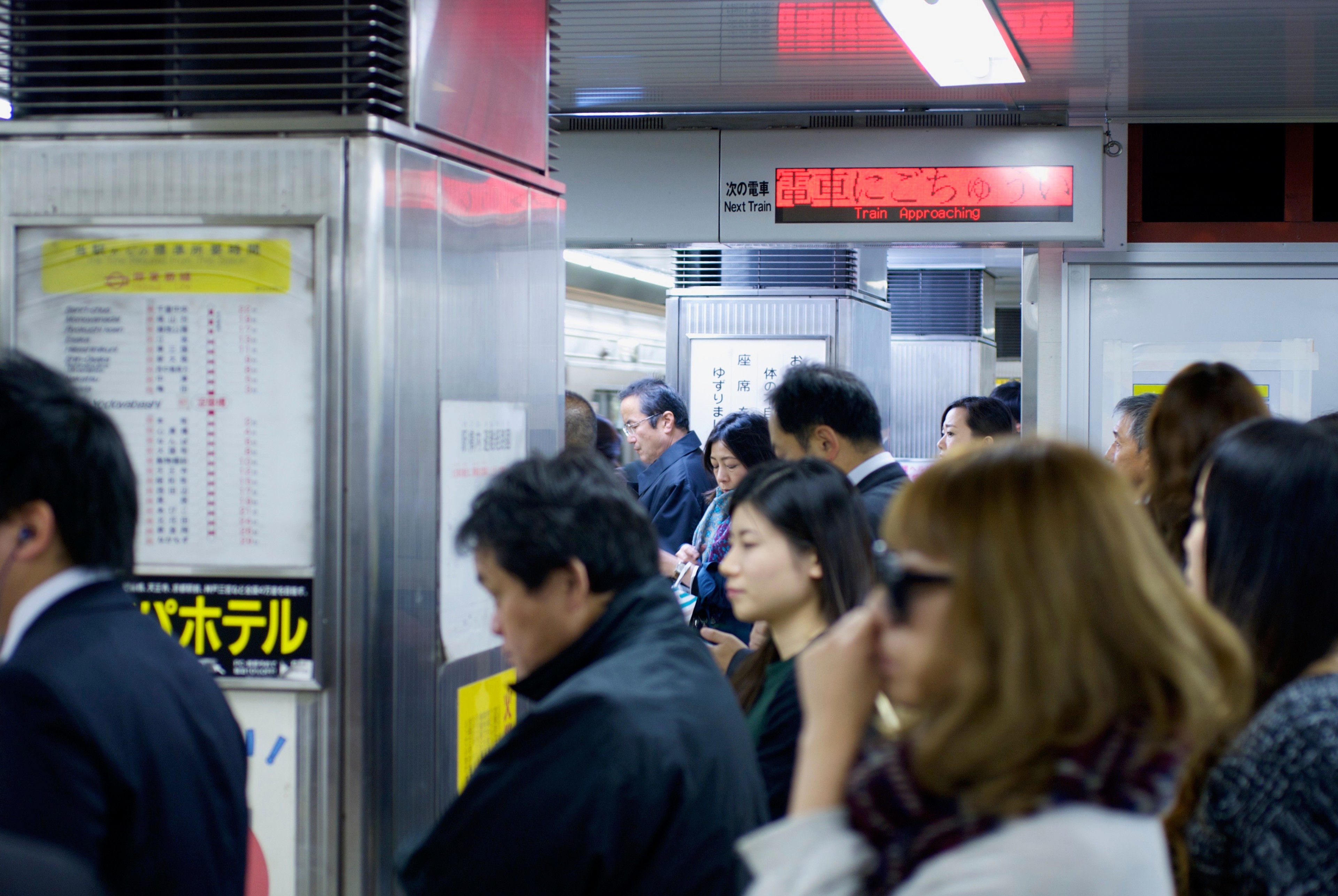 Commuters wait on a train platform beneath station signs.