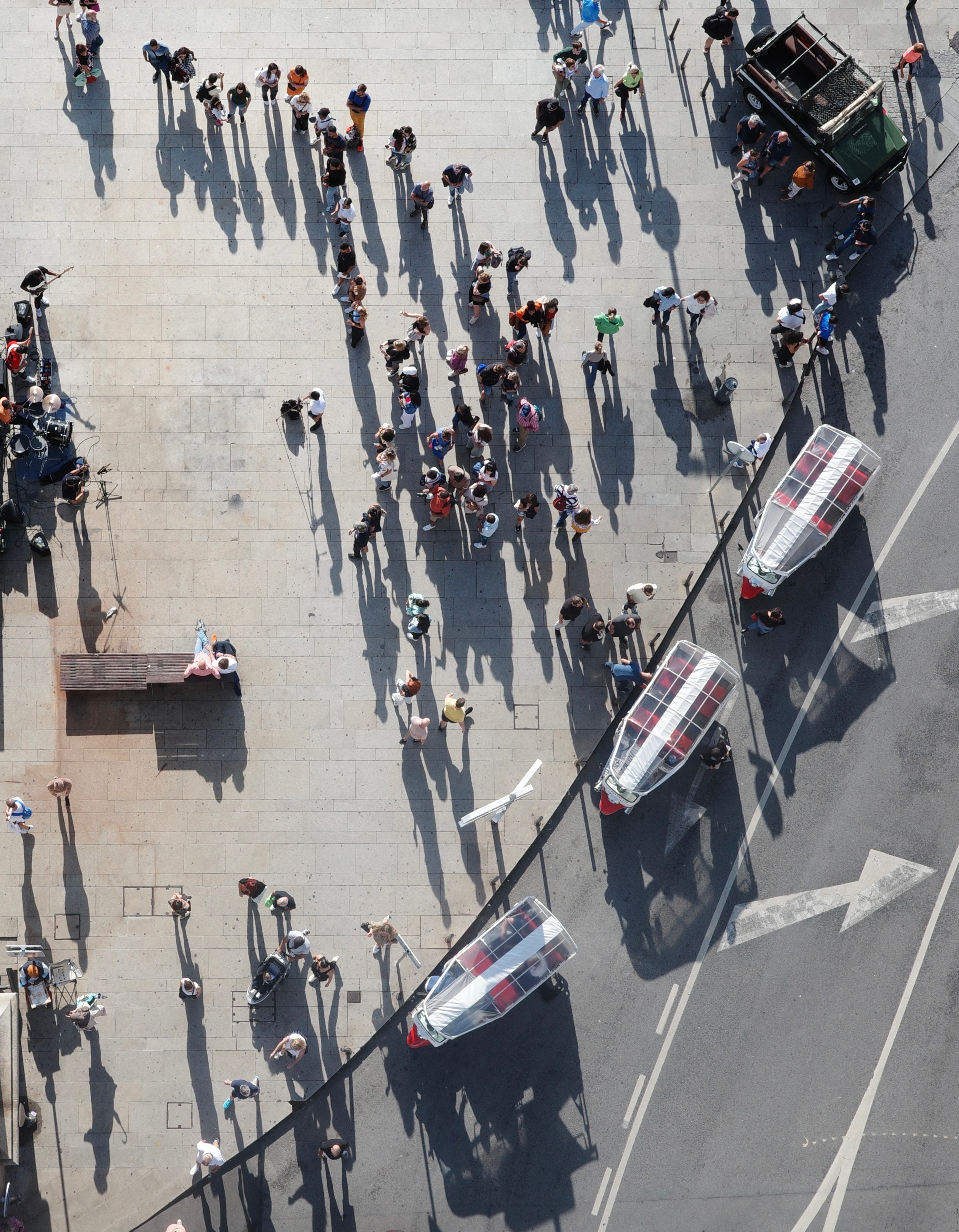 People cast long shadows across a riverside plaza beside a boat.