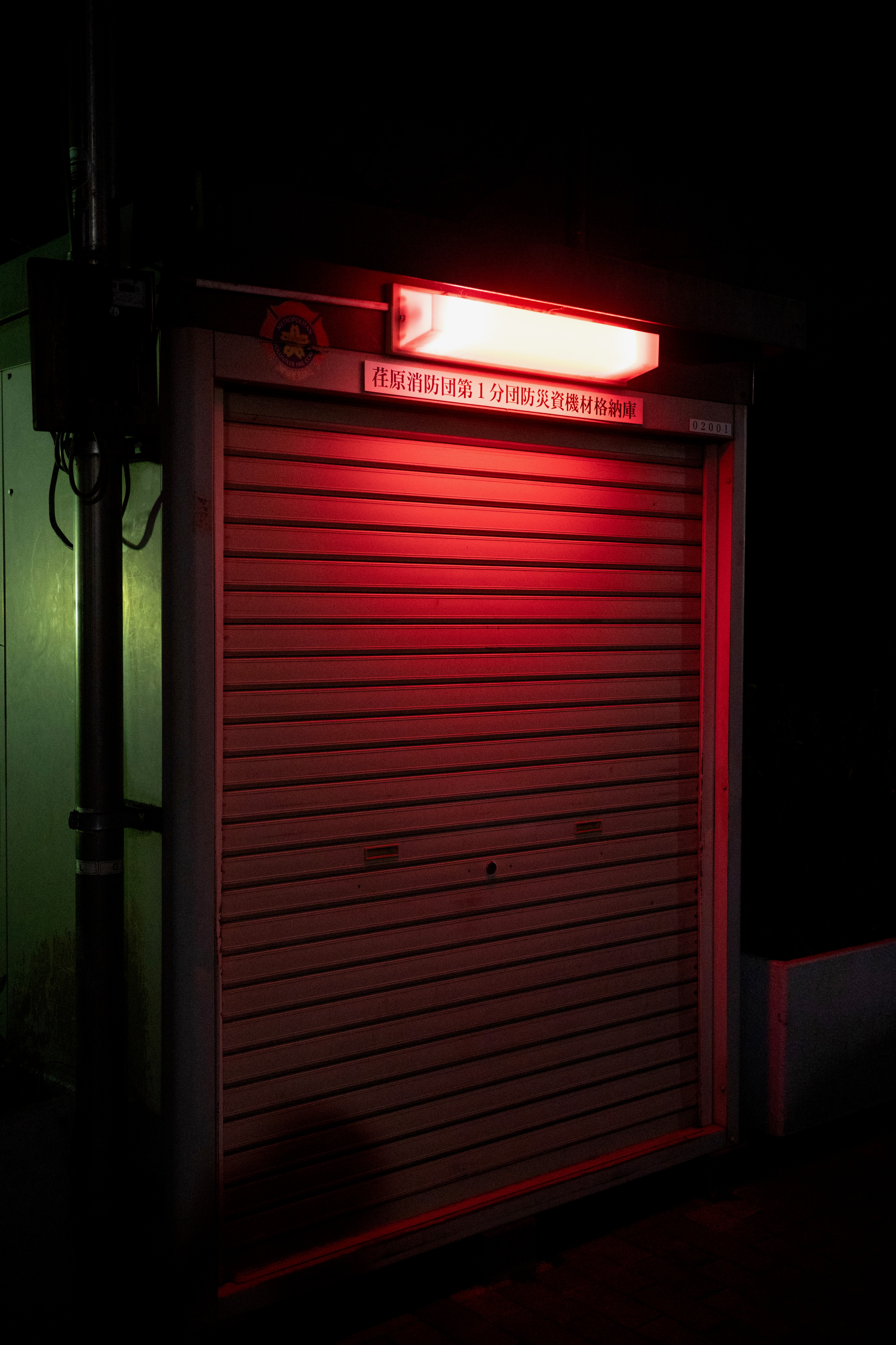 A closed red shutter glows under a streetlight.