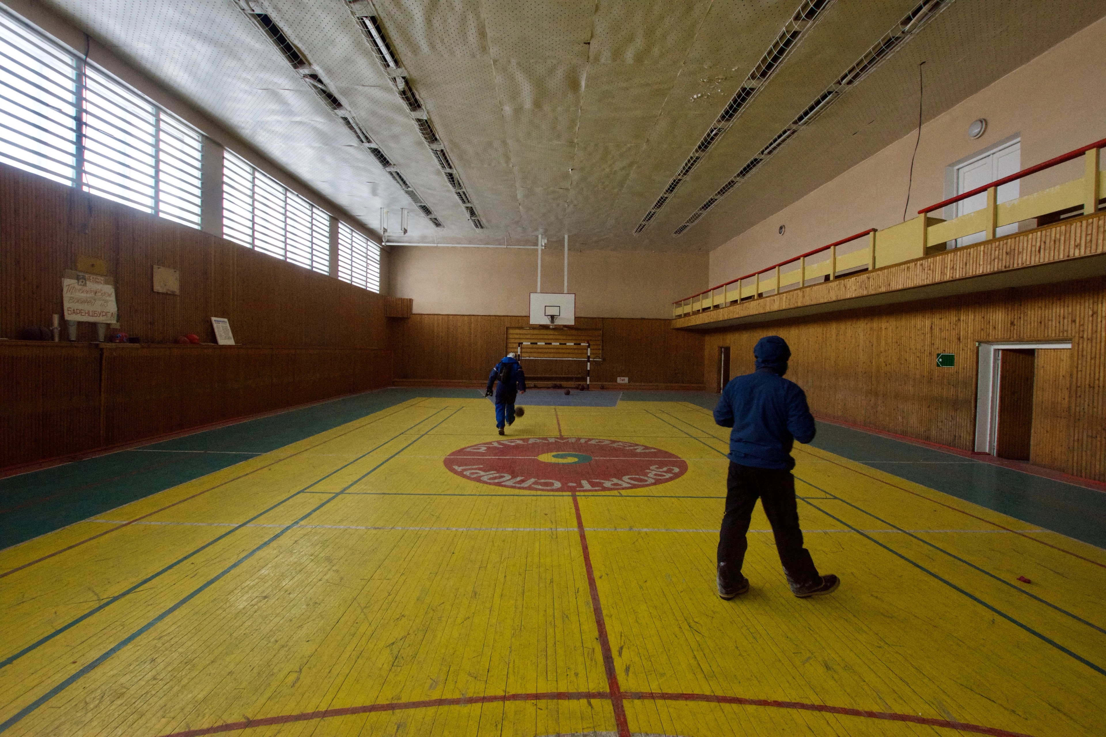 Two people walk across the floor of an indoor sports hall.