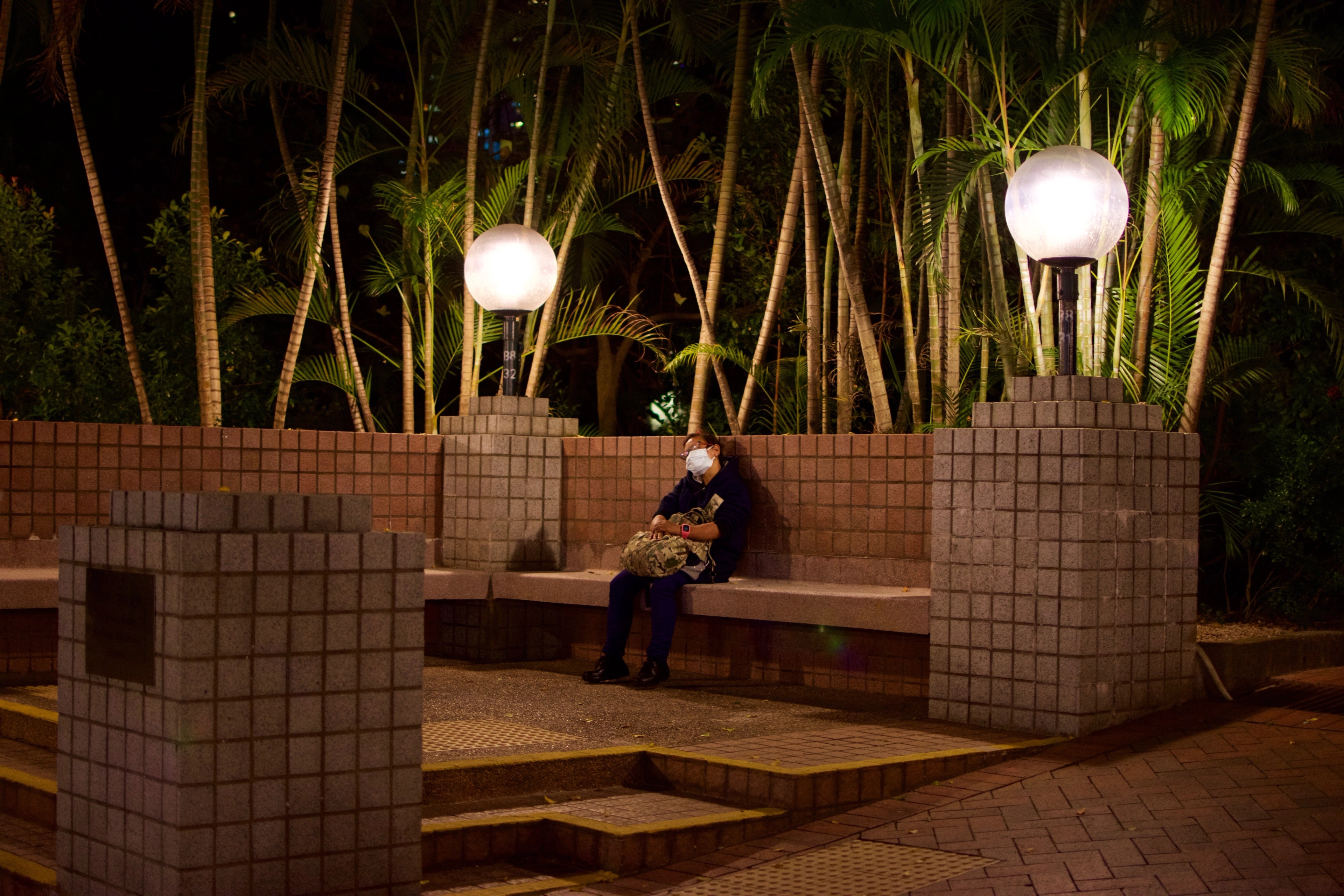 A person sits on stepped benches beneath round garden lights.