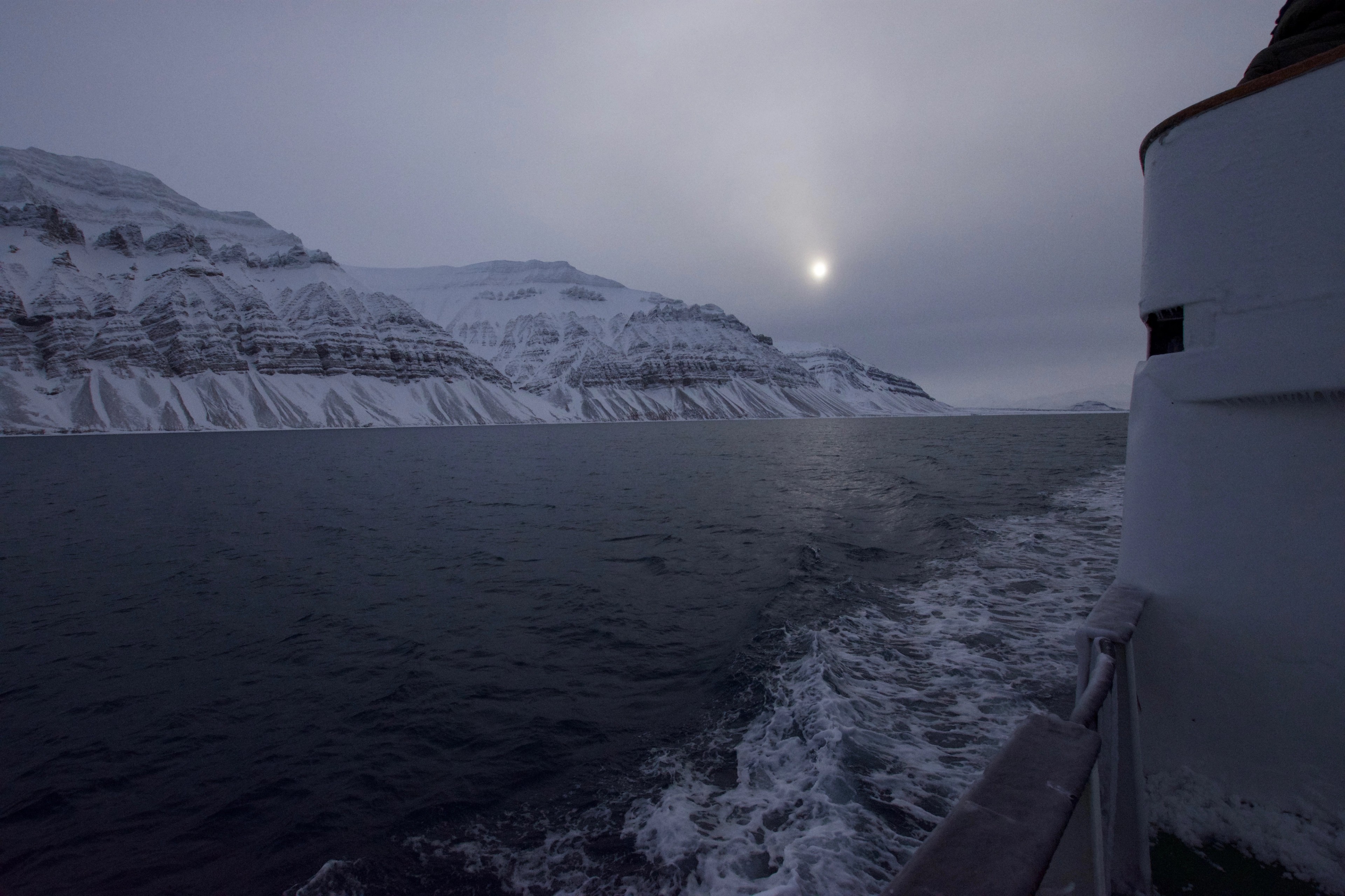 A boat travels along the edge of a snowy coastline.