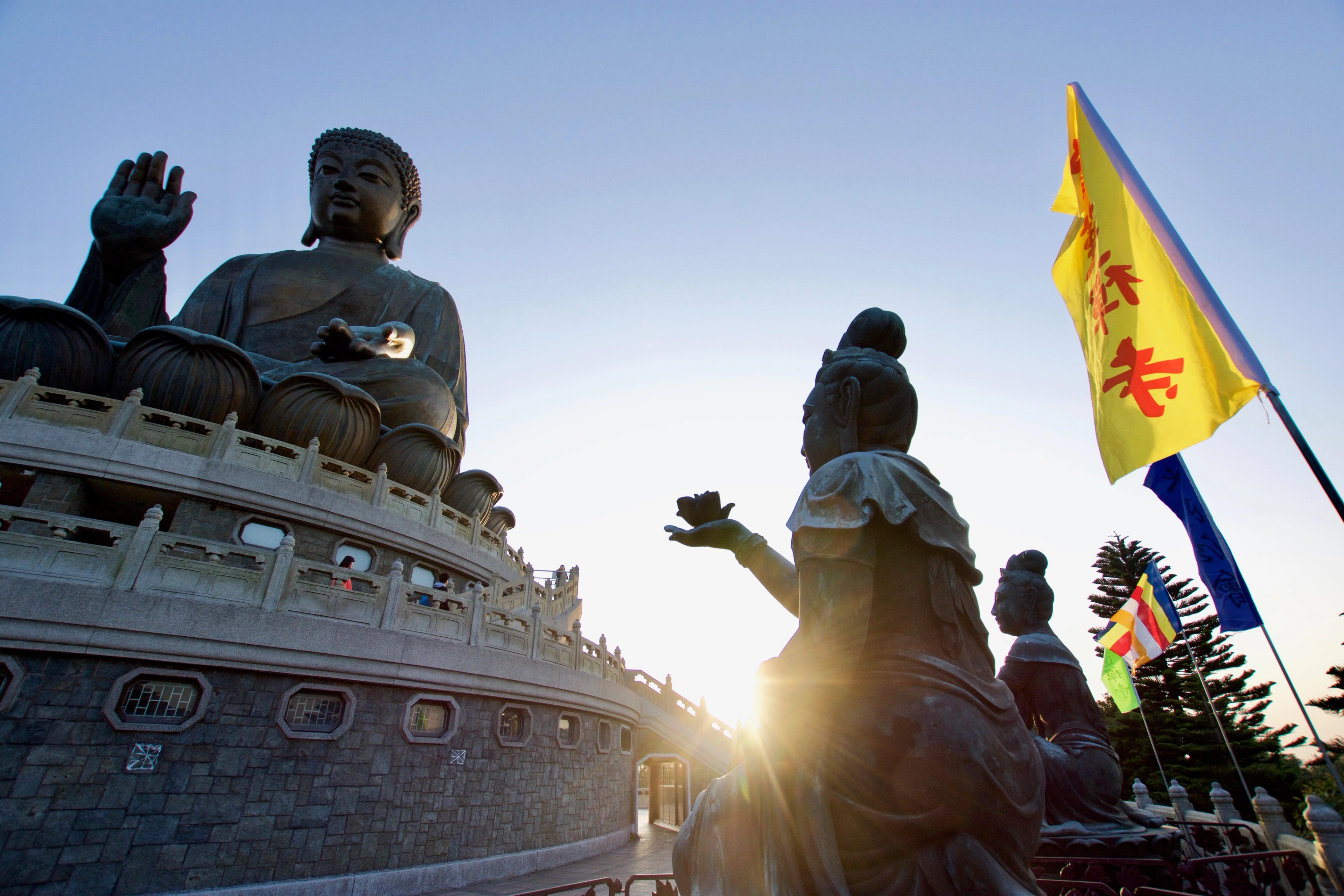 Large bronze statues stand above a temple plaza in the low sunlight.