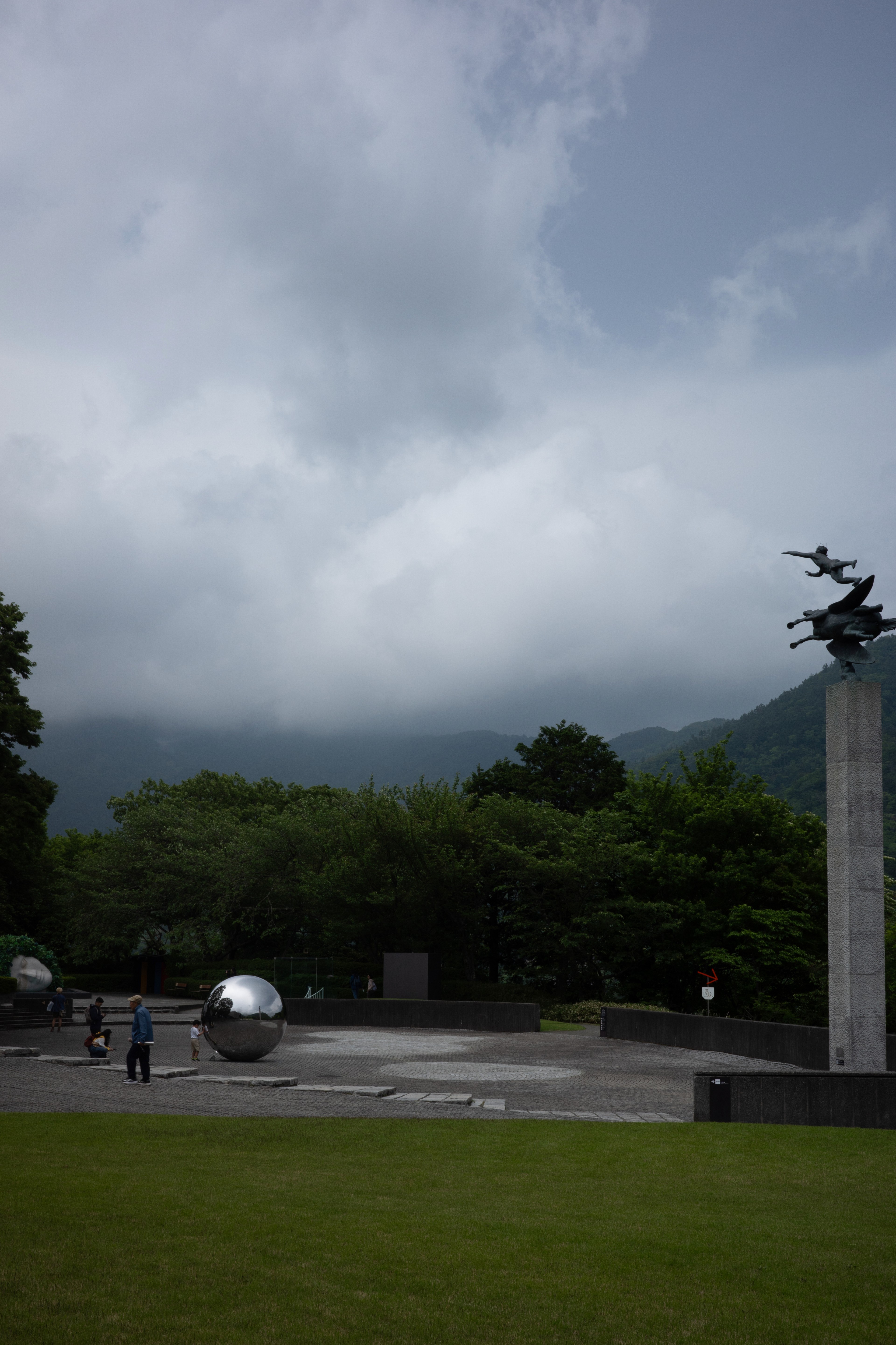 Clouds hang above a low stone wall and tree-lined park.
