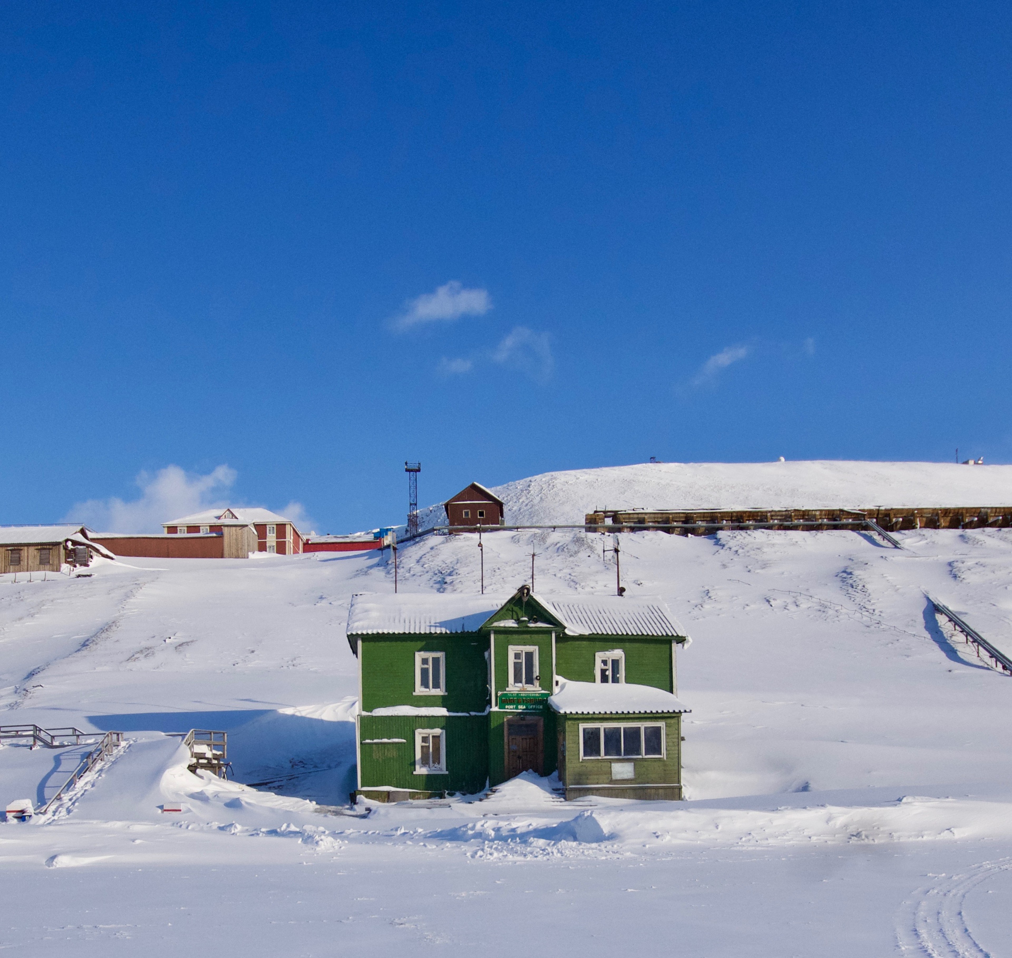 A green house stands among colorful buildings and snow.