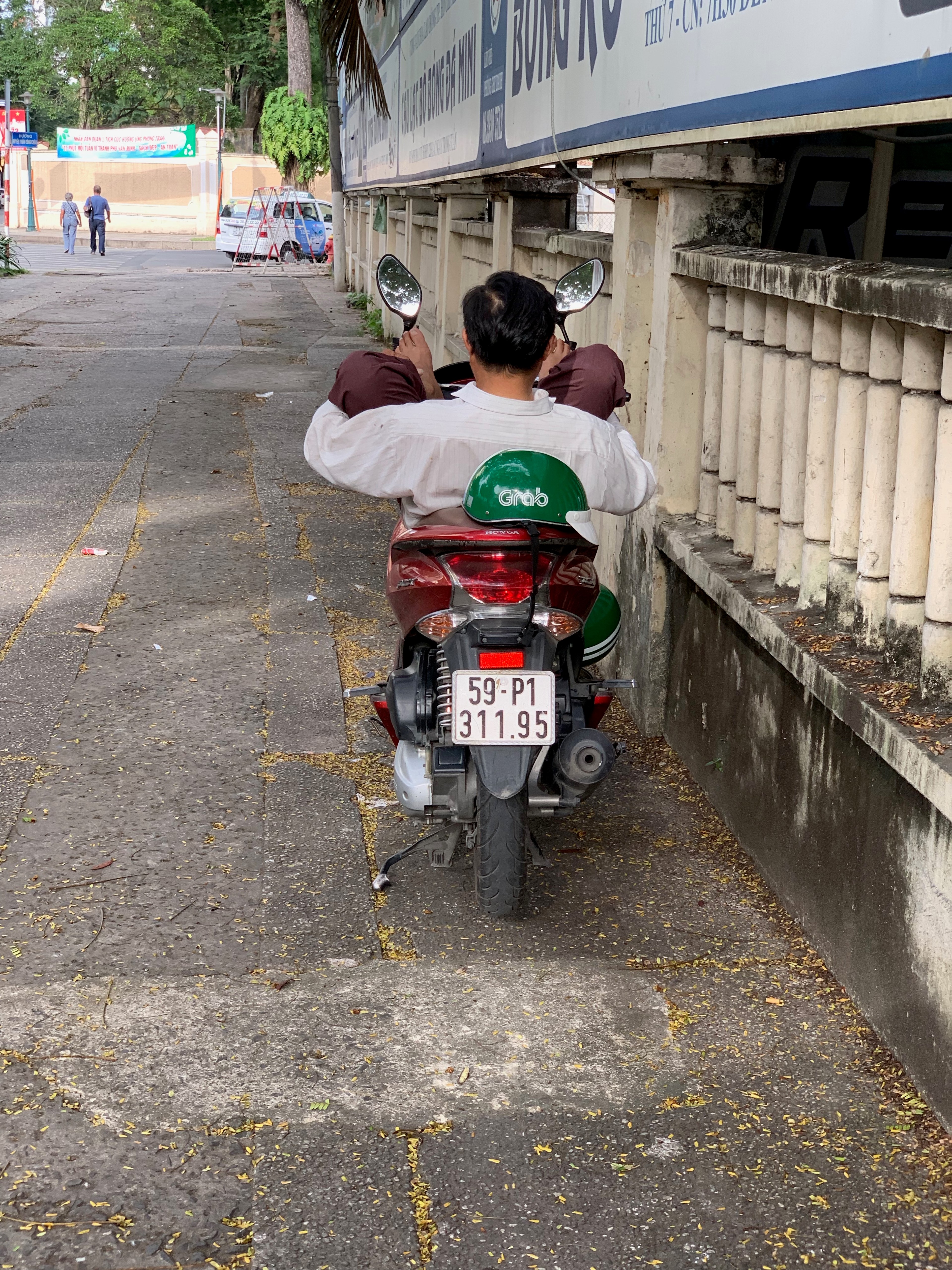 A motorbike rider waits beside the sidewalk and a low railing.
