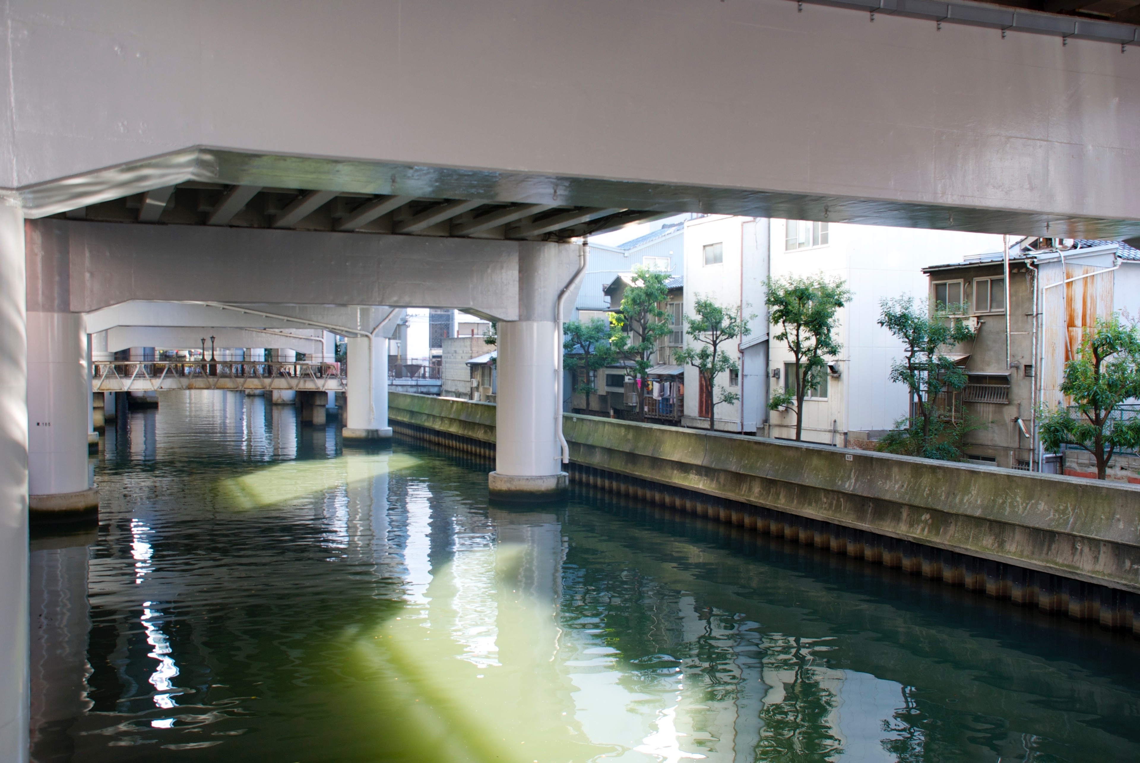 A narrow canal flows beneath an elevated roadway and city buildings.