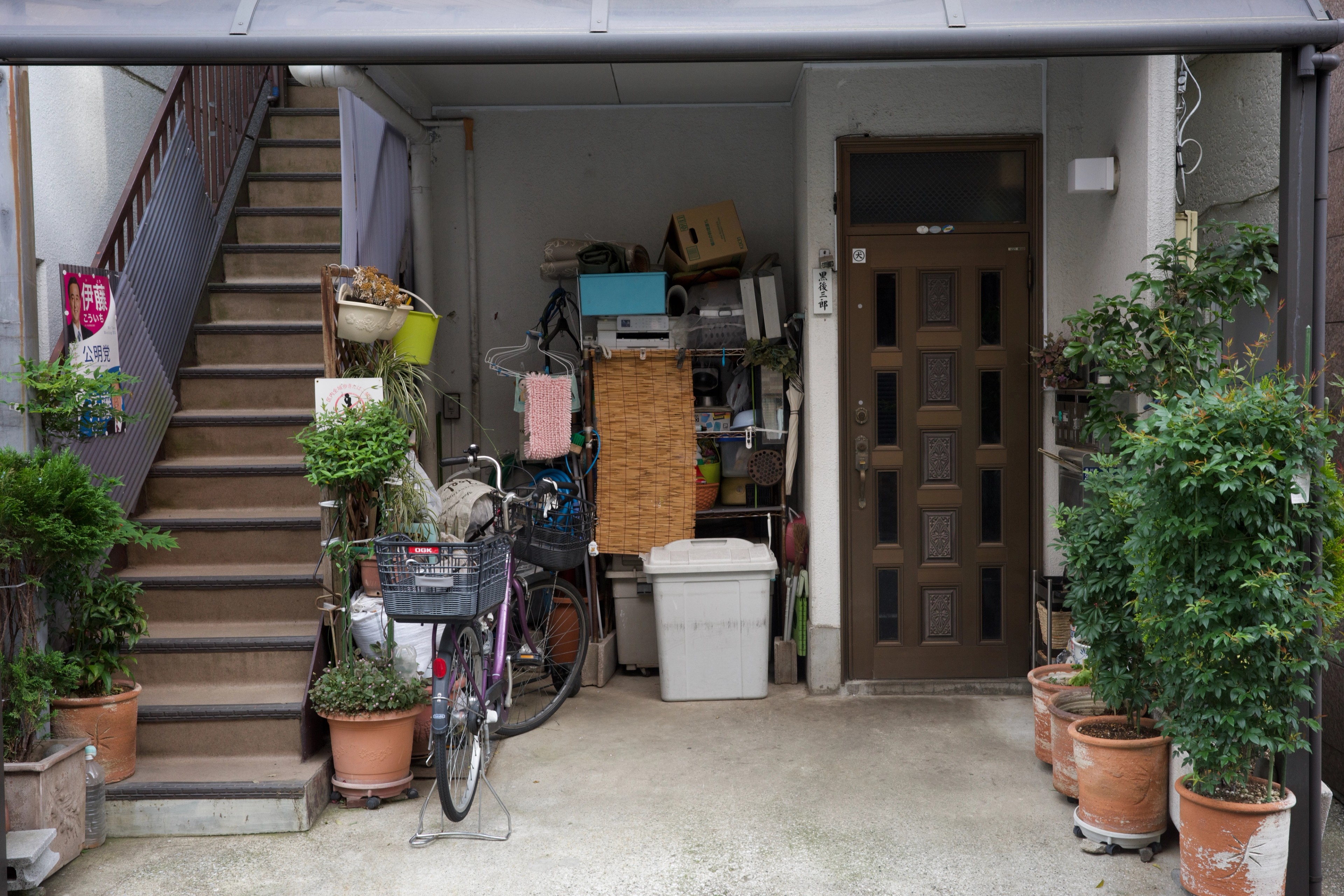 A crowded residential entrance with a bicycle and potted plants.