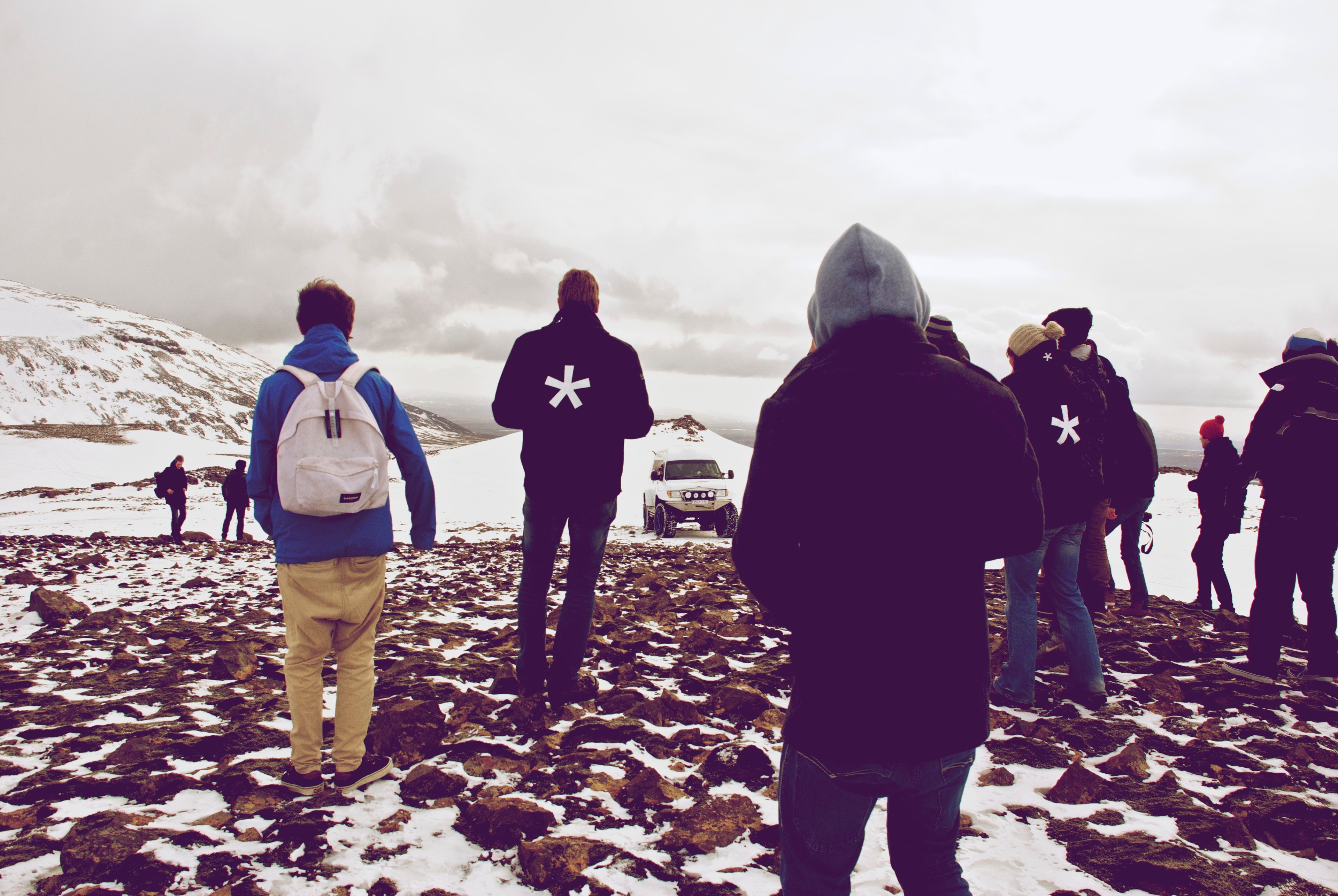 People in colorful jackets walk across a rocky snow-covered plain.