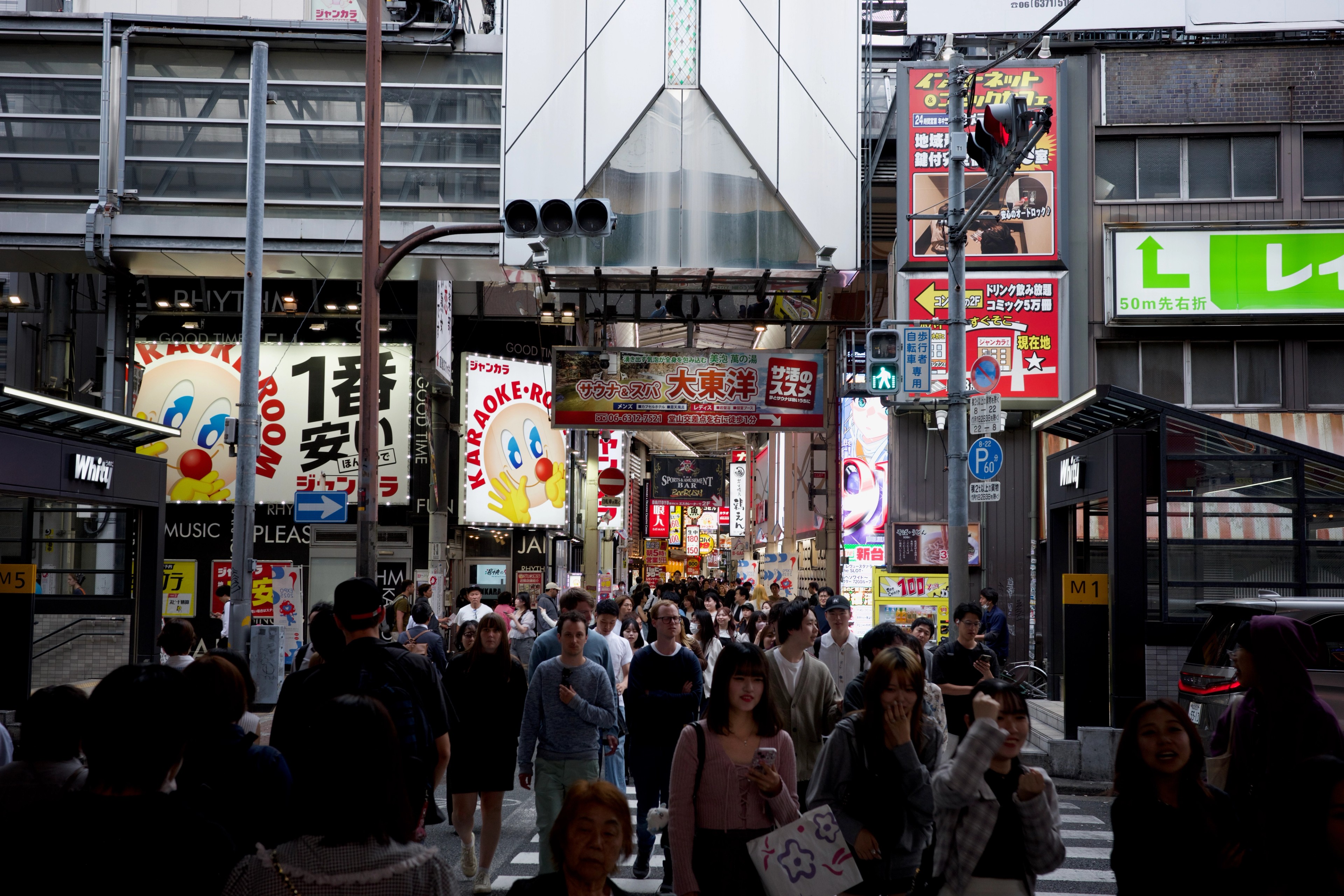 Crowds fill an intersection among tall buildings and signs.