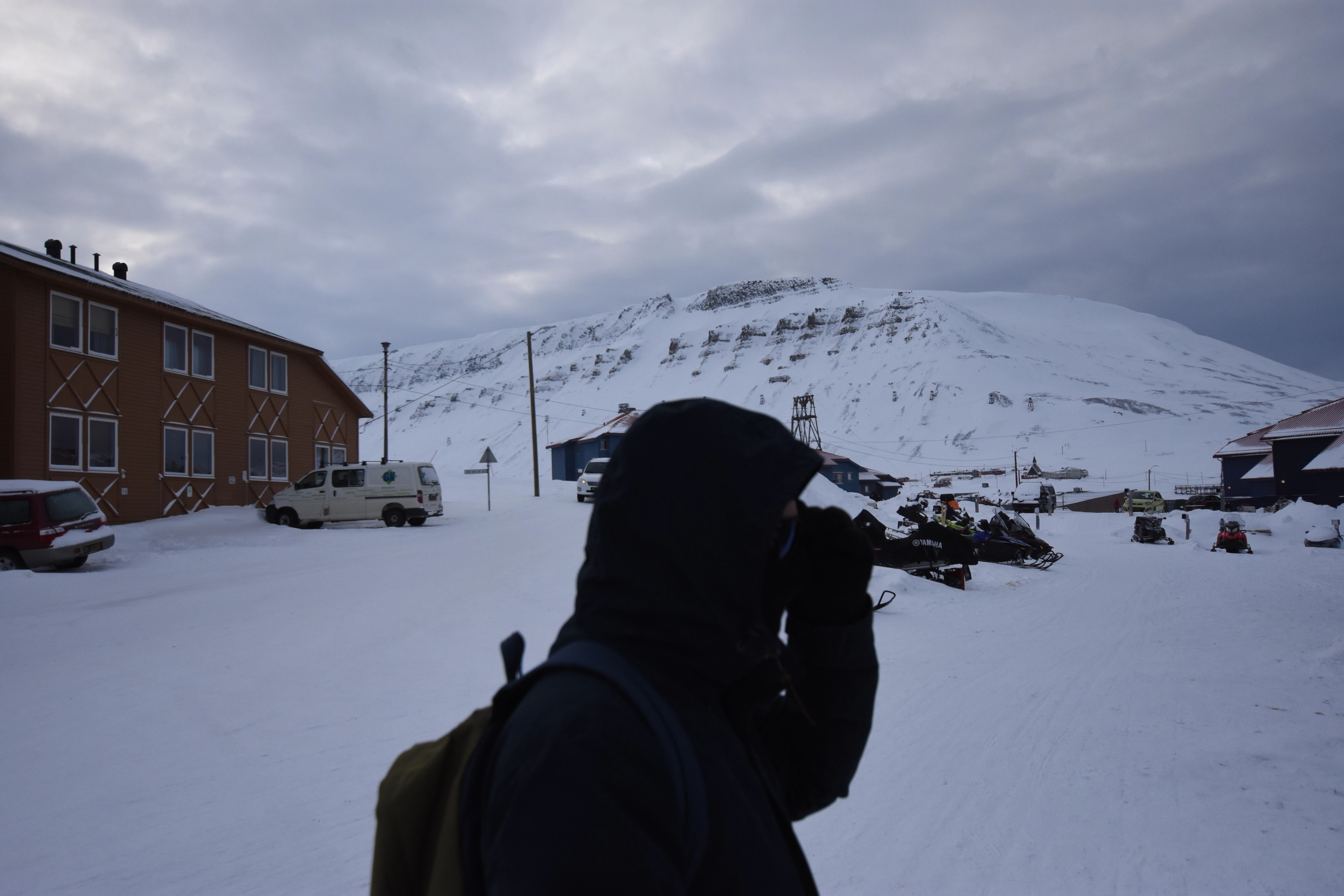 A person stands in a snow-covered settlement beneath a mountain.
