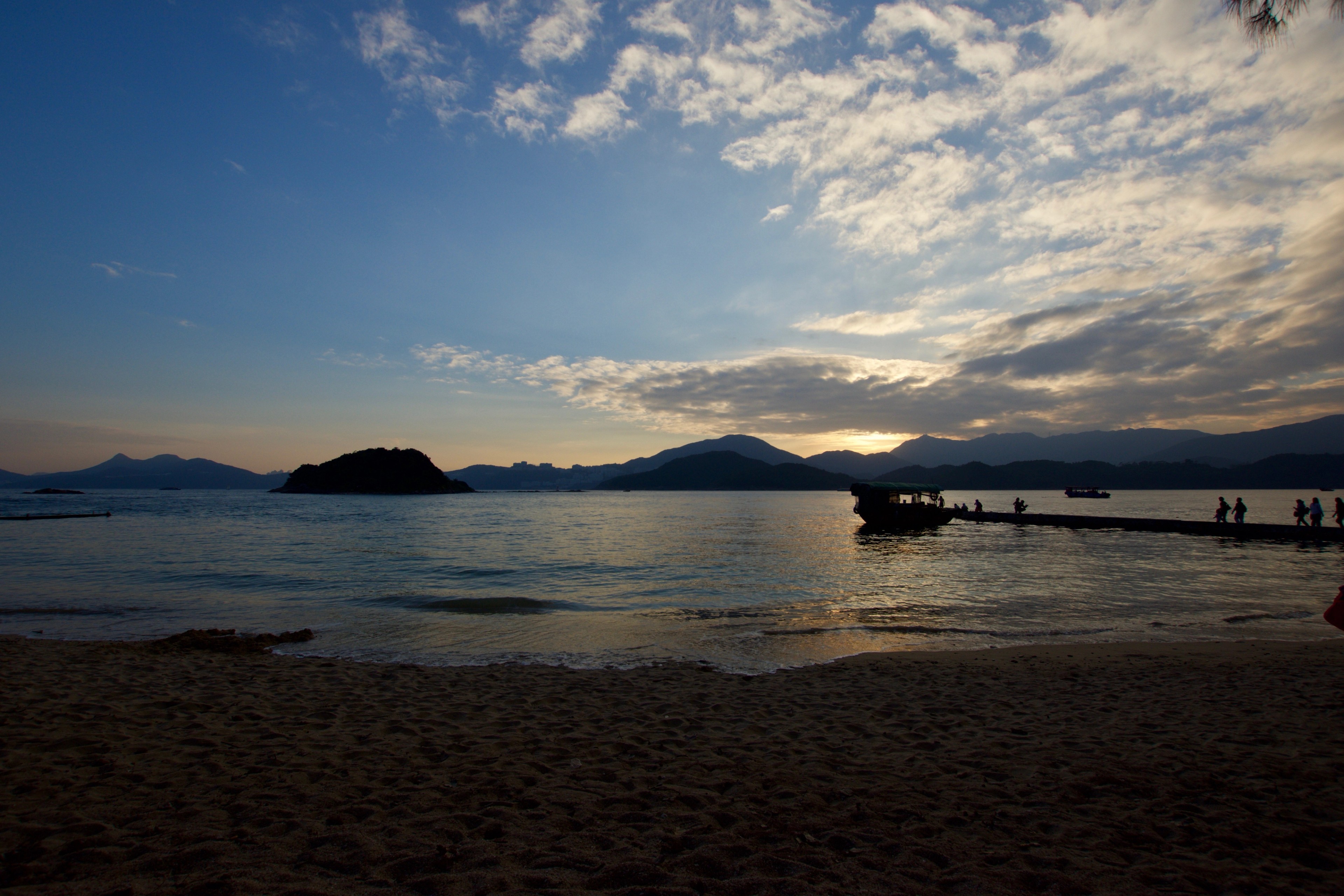 The setting sun glows over a quiet beach and distant islands.