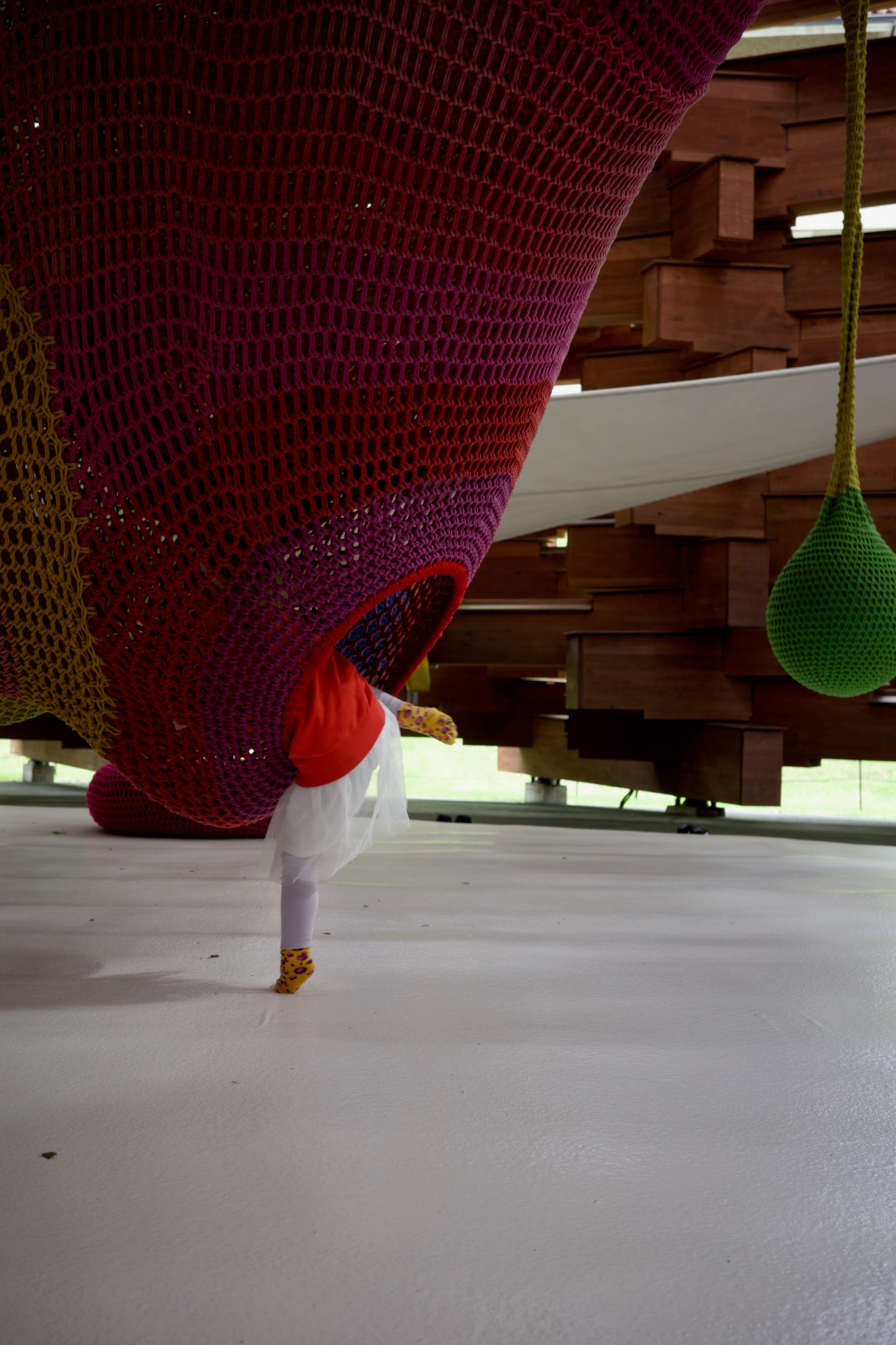 A close view of a red curved sculpture and green hanging form above a child.