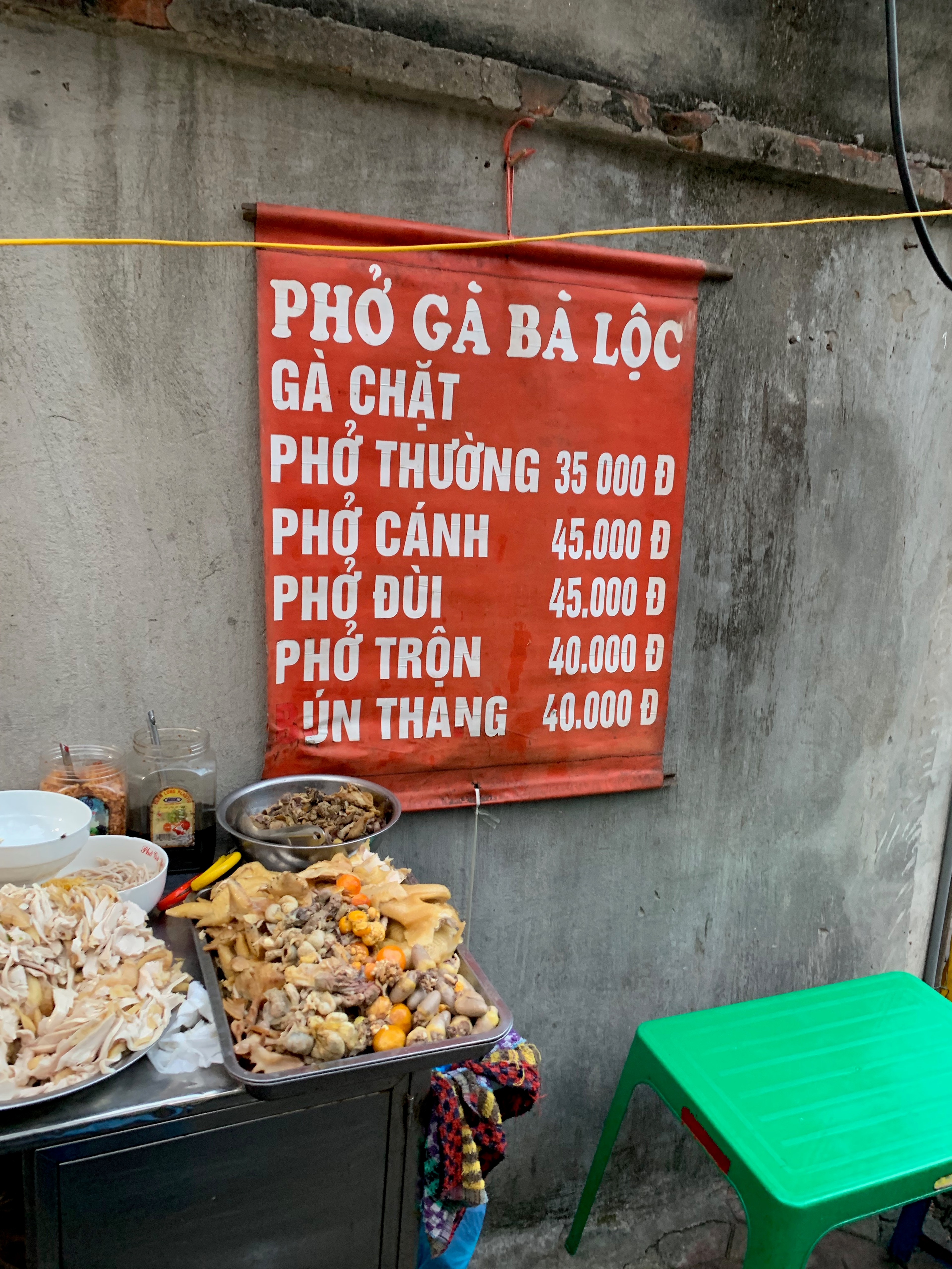 A red Vietnamese menu board hangs above a small sidewalk food stall.