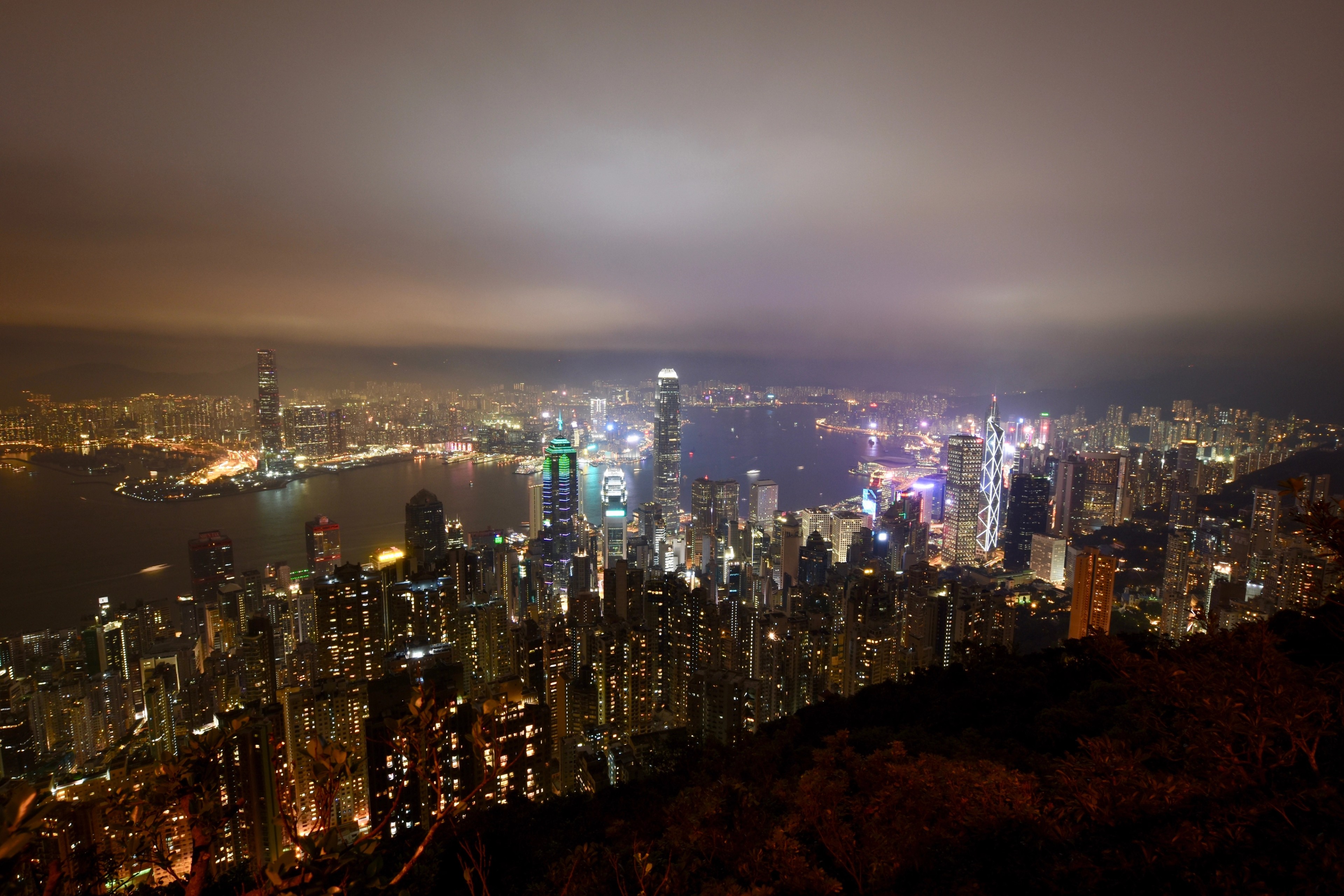 Hong Kong skyscrapers glowing at night, viewed from a hillside.