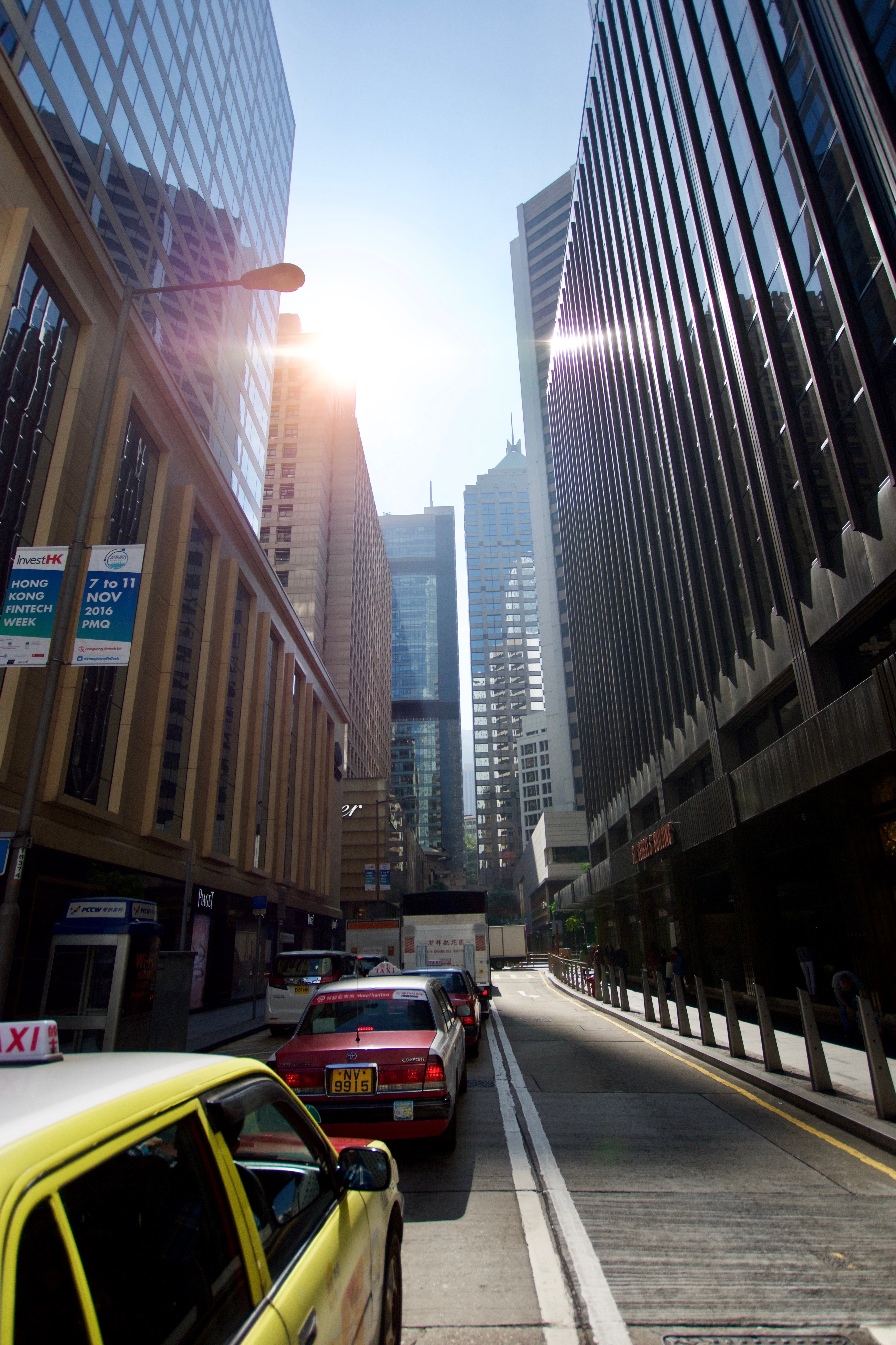 A yellow taxi drives through a narrow street canyon of tall buildings.