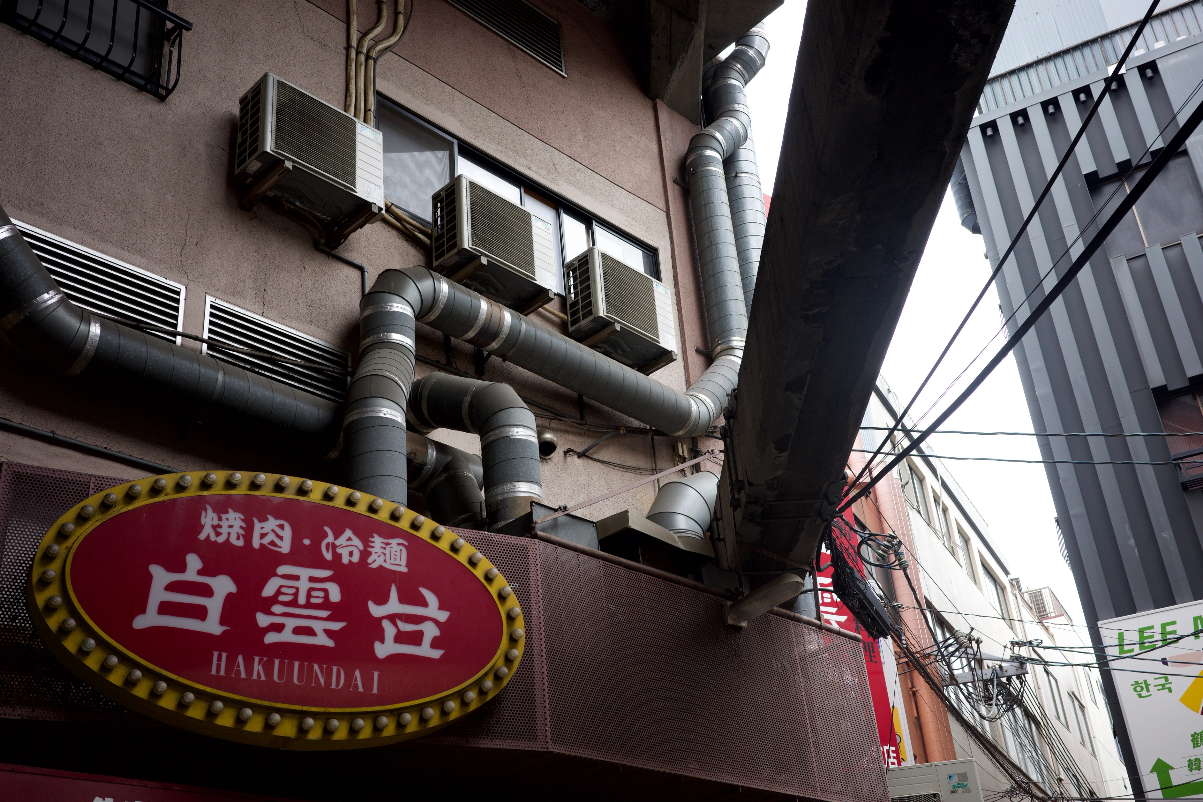 A restaurant sign and pipes beneath city buildings.