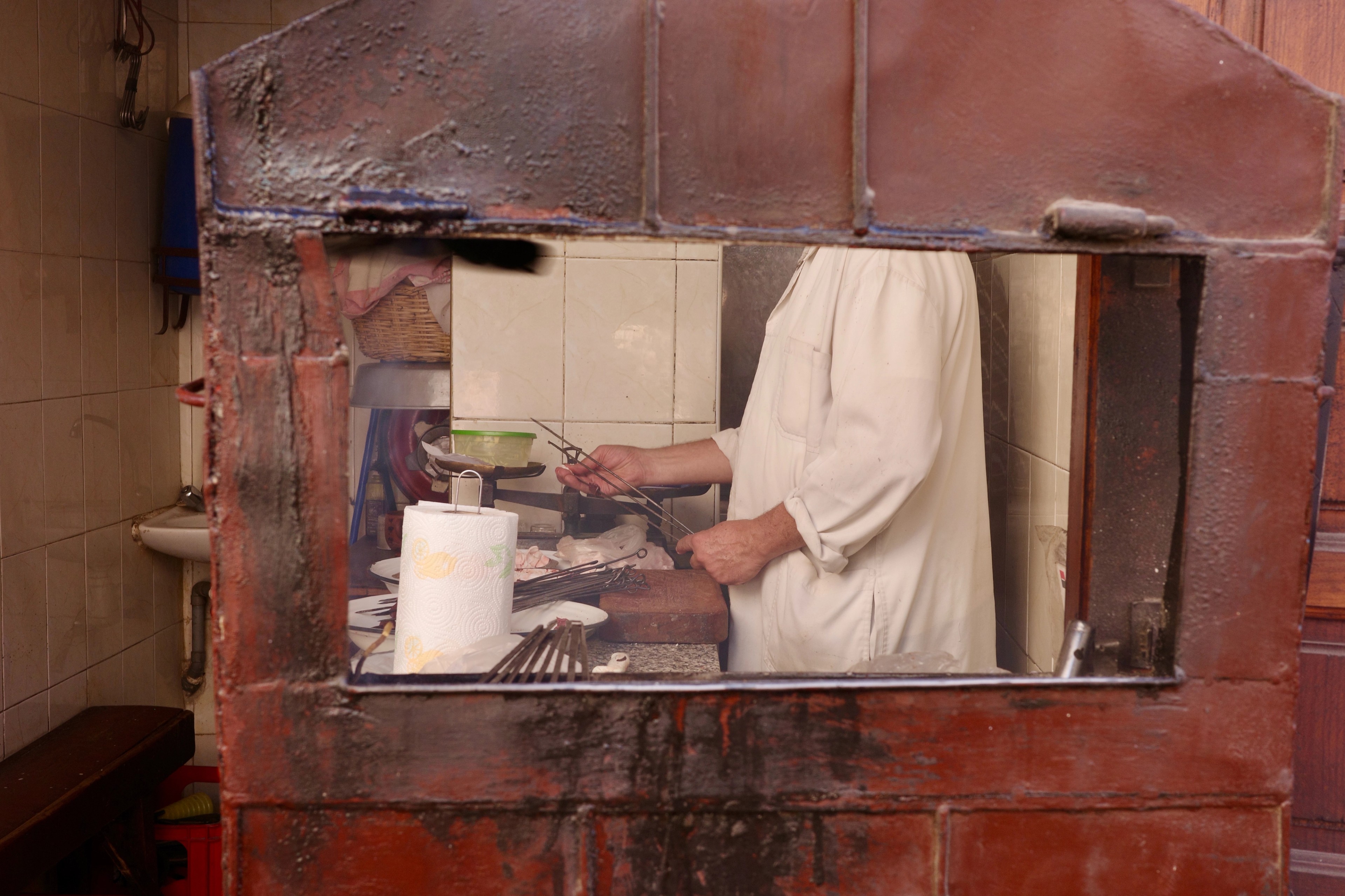 A cook works at a counter, seen through a square opening in the wall.