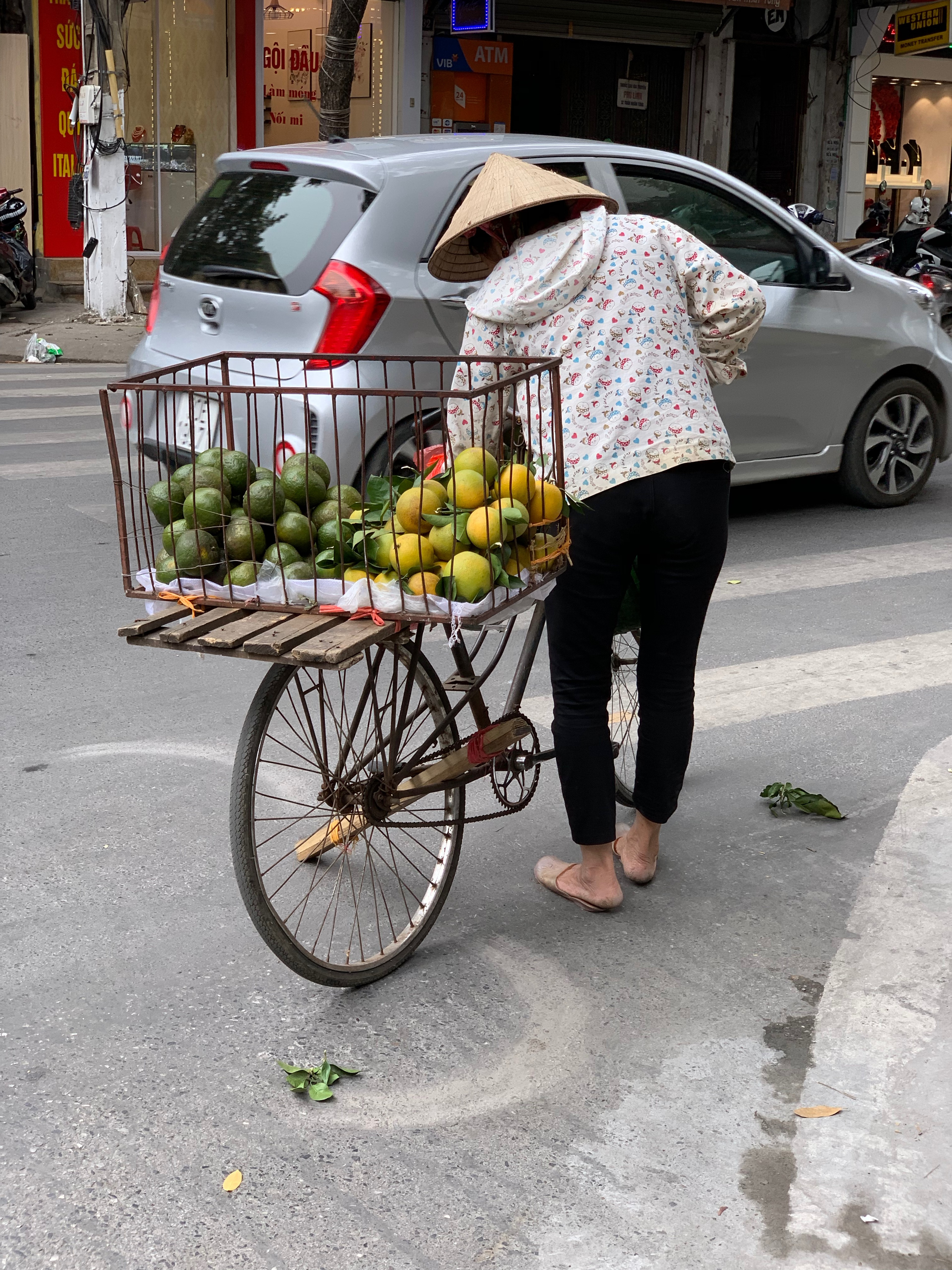 A person bends over a bicycle loaded with baskets of fruit.