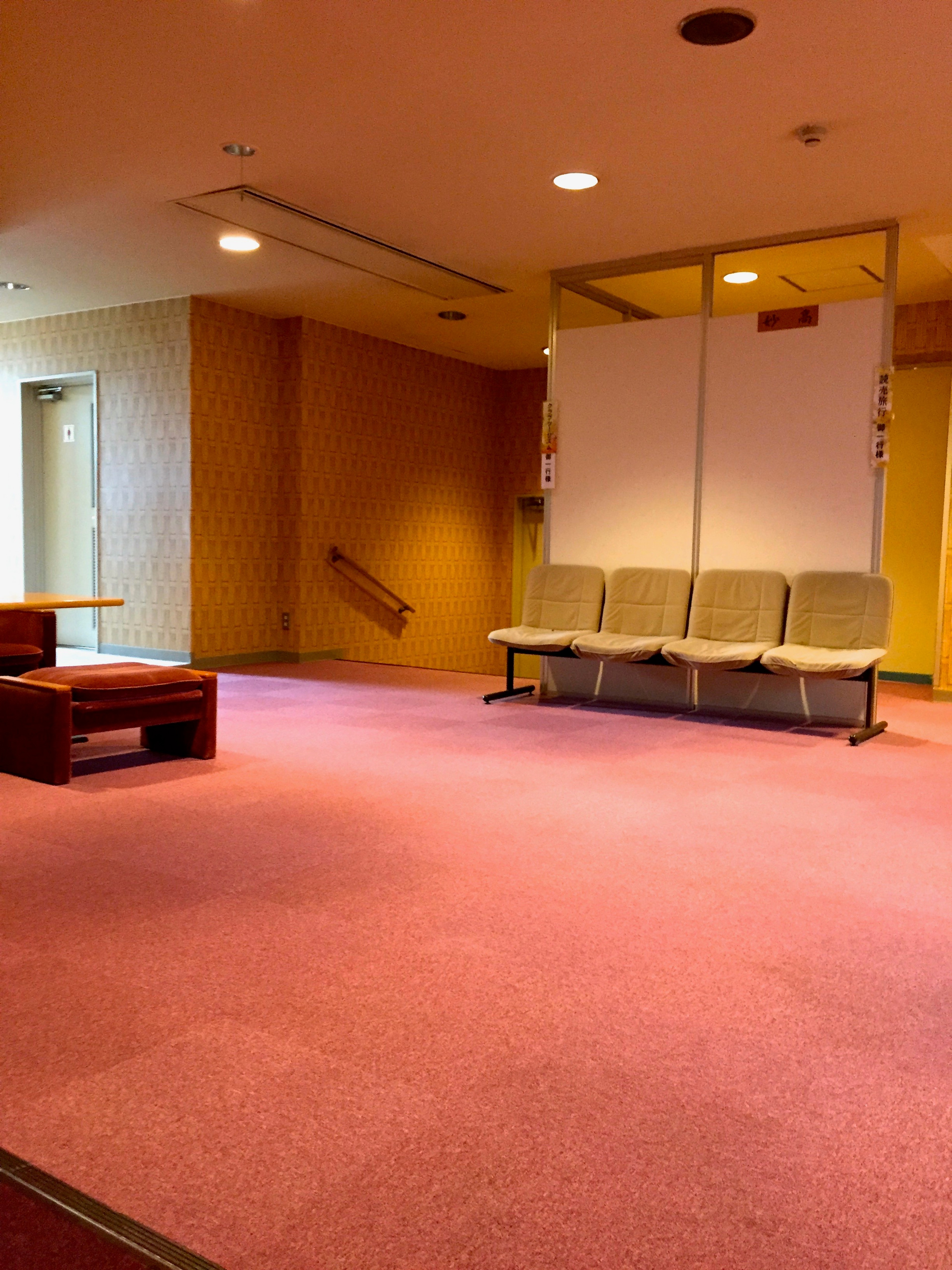 An empty room with salmon-colored carpet and a low seating area.