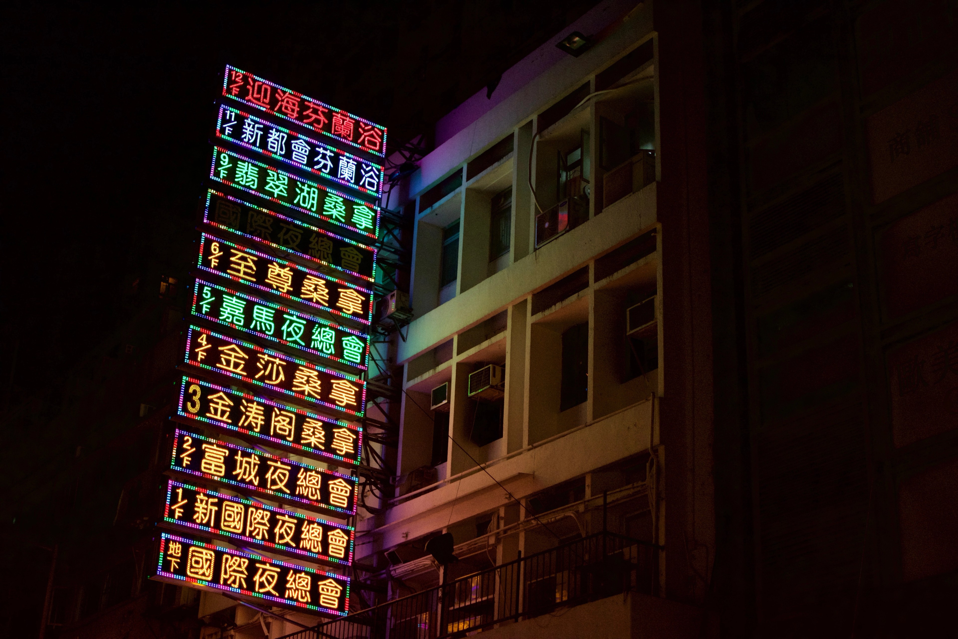 A brightly lit column of Chinese-language signs stands against a dark building.