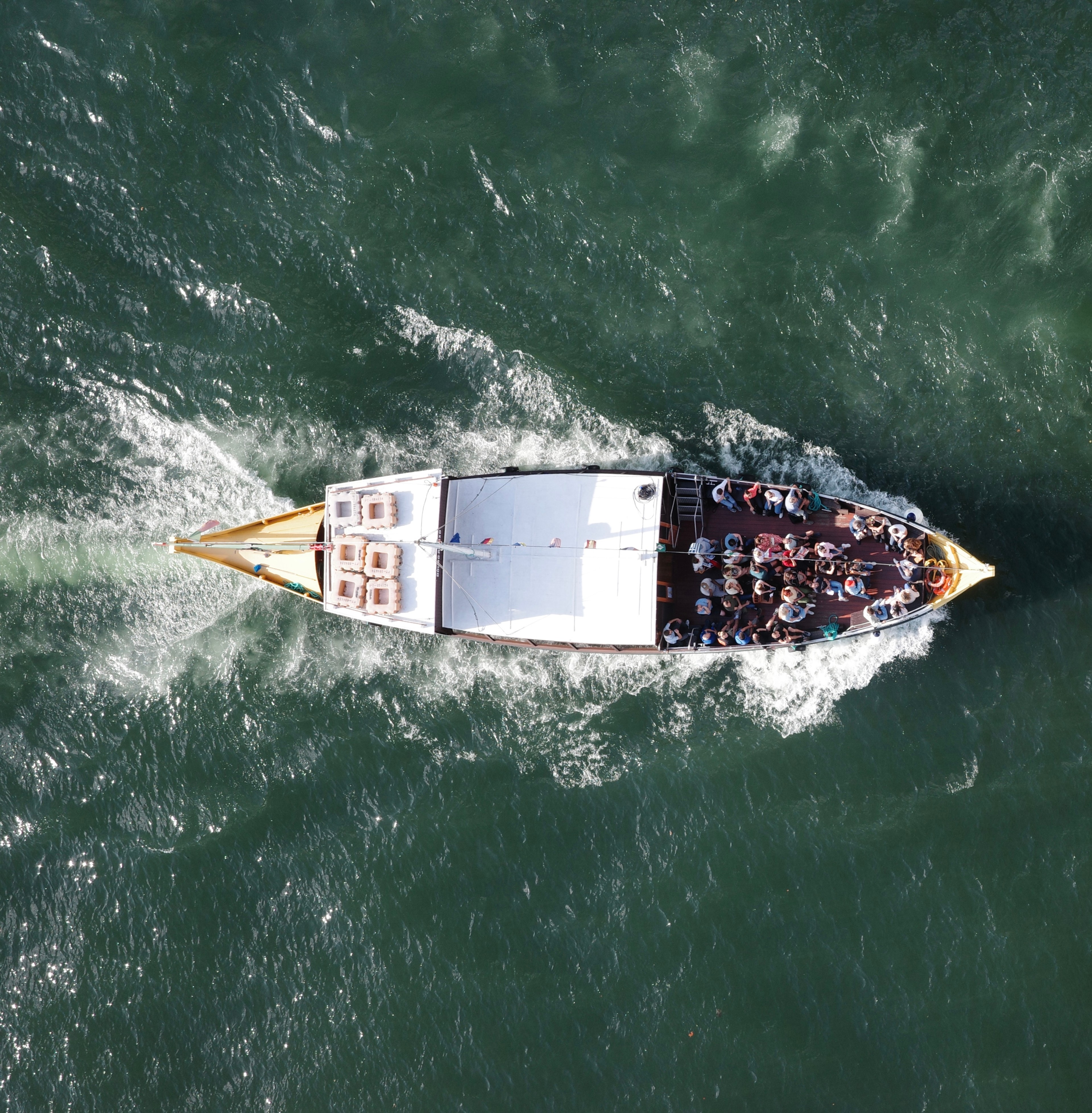 A long boat cuts through green water, leaving a bright white wake.