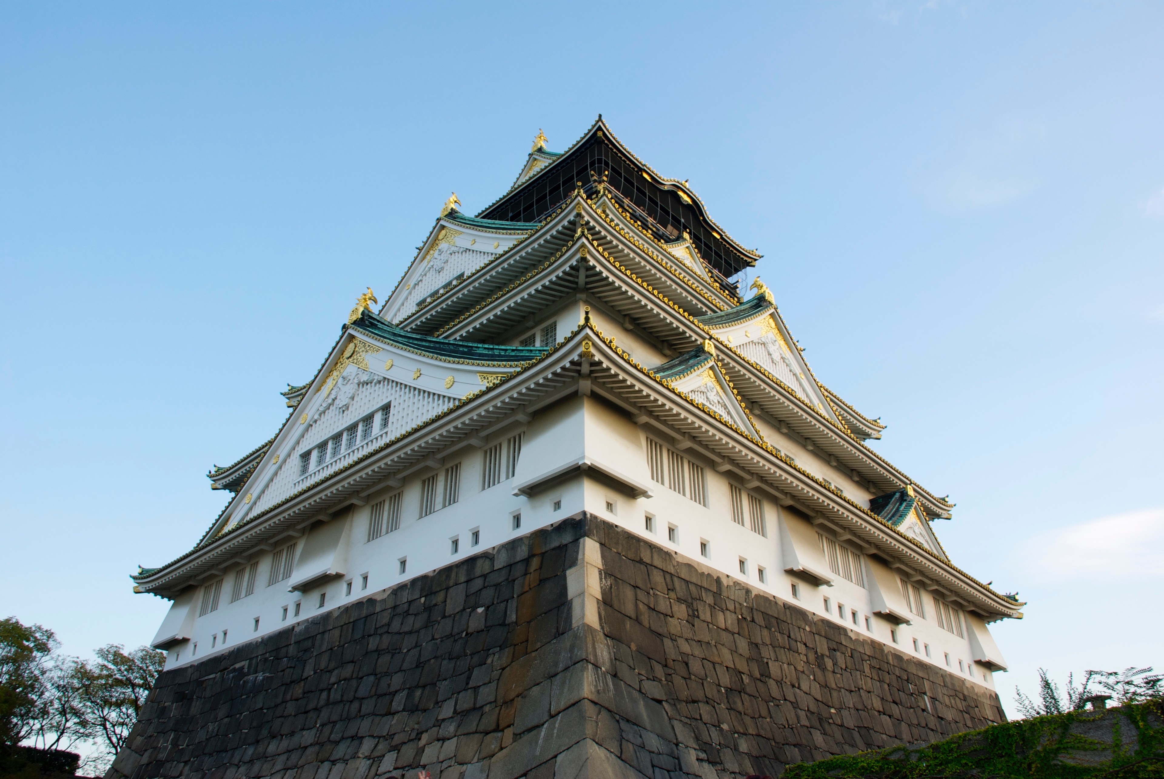 Osaka Castle’s white walls and green roof rise above stone walls and trees.