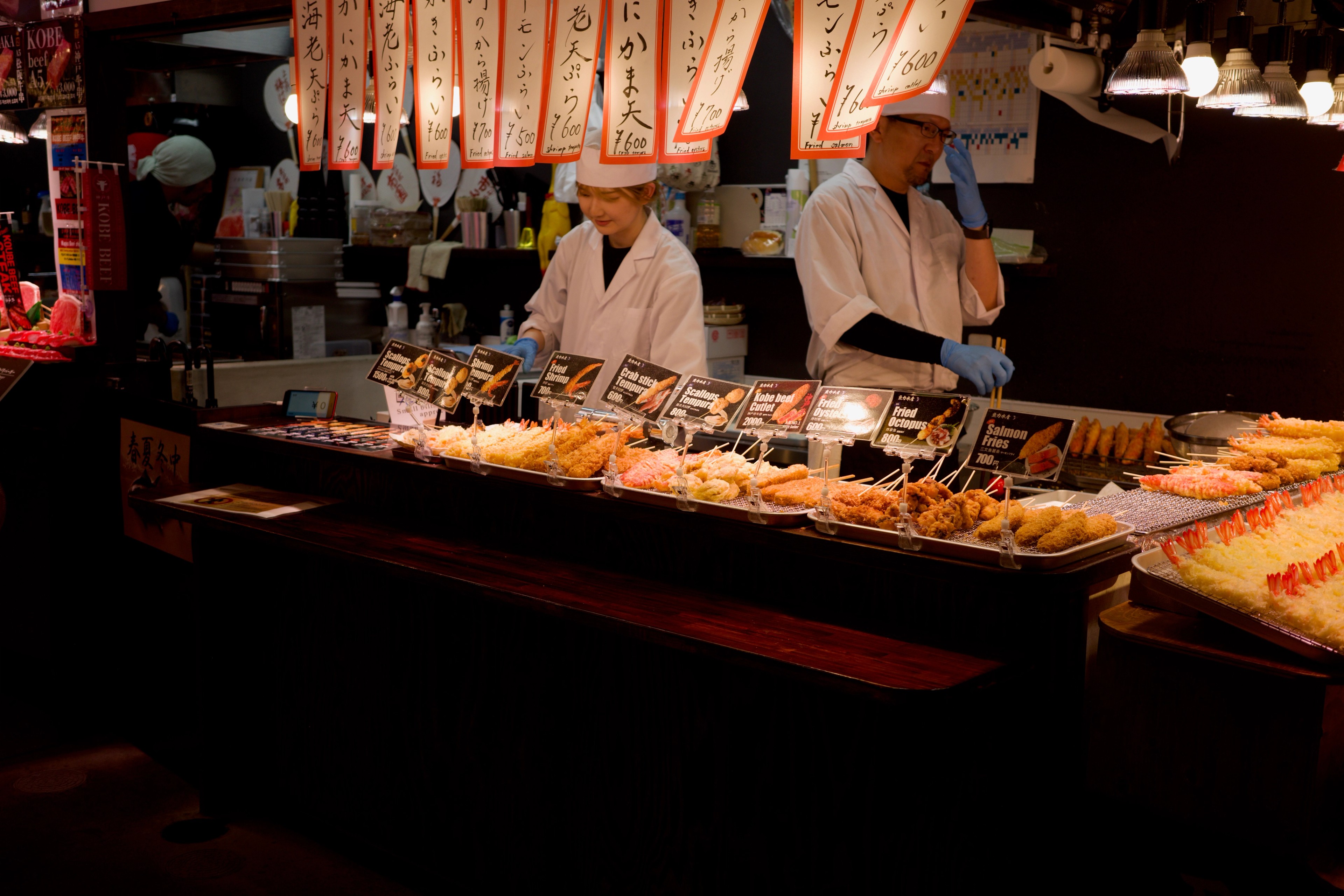 A market vendor stands behind a counter of fried foods.