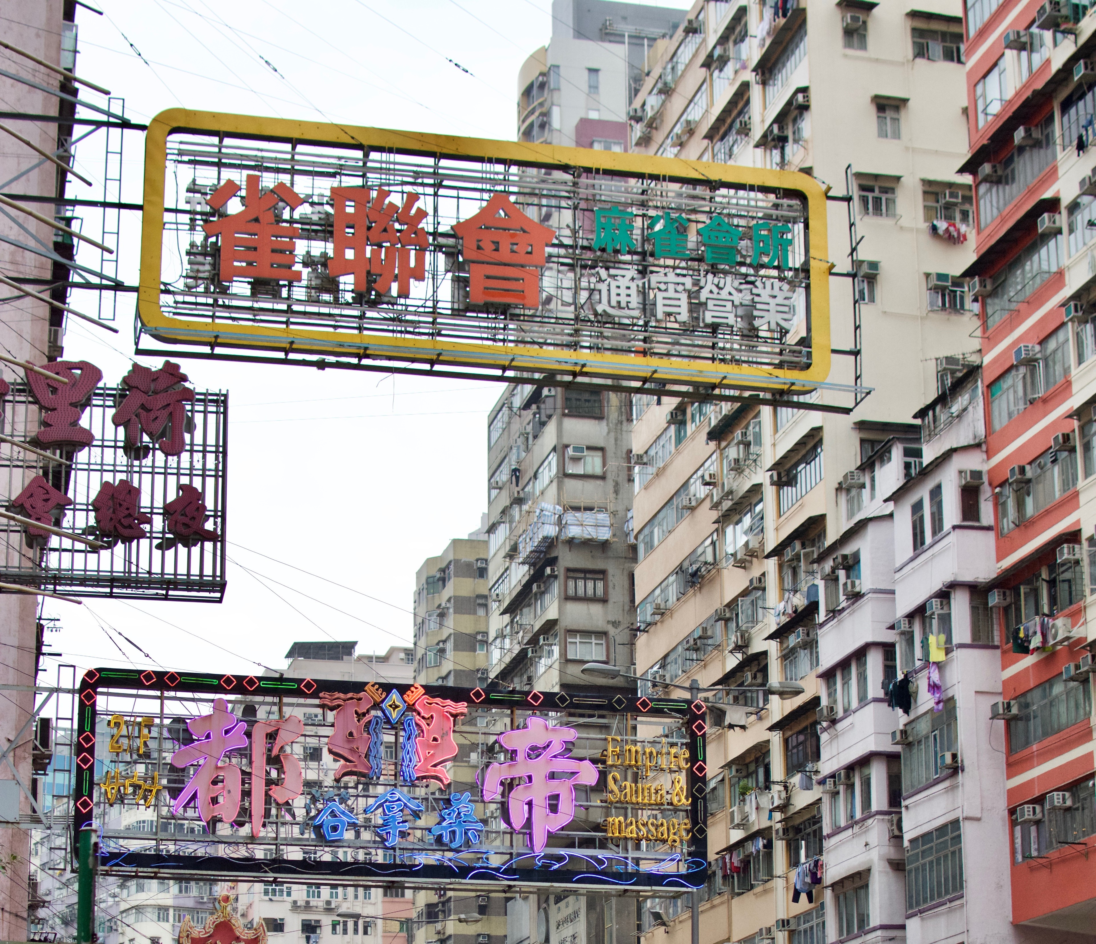 Layers of Chinese shop signs hang above a busy Hong Kong street between tall apartment buildings.