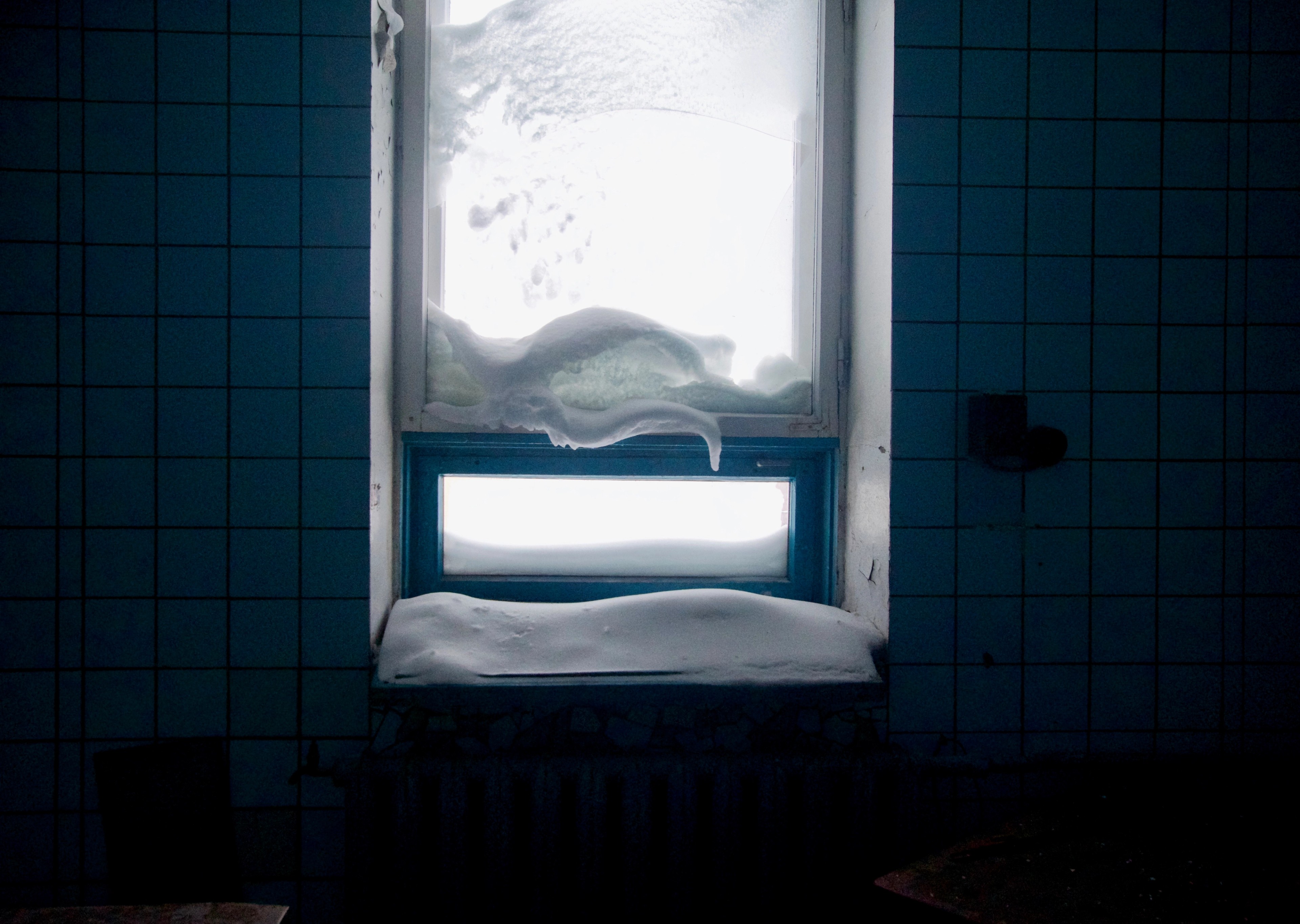 A frosted window above a tiled basin in a blue-tiled room.
