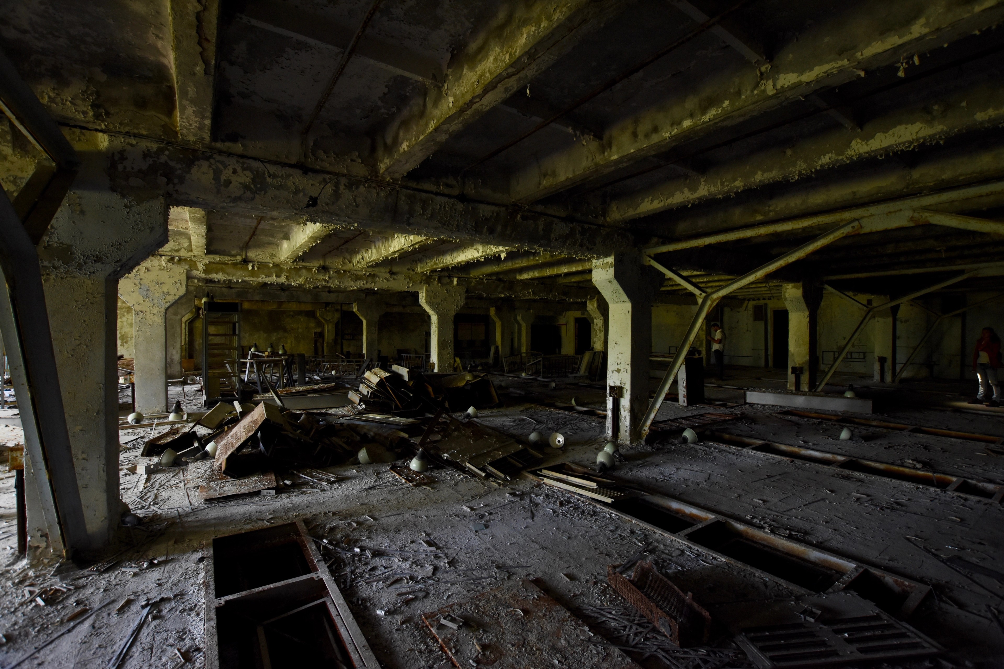 An abandoned industrial hall with concrete columns and debris.
