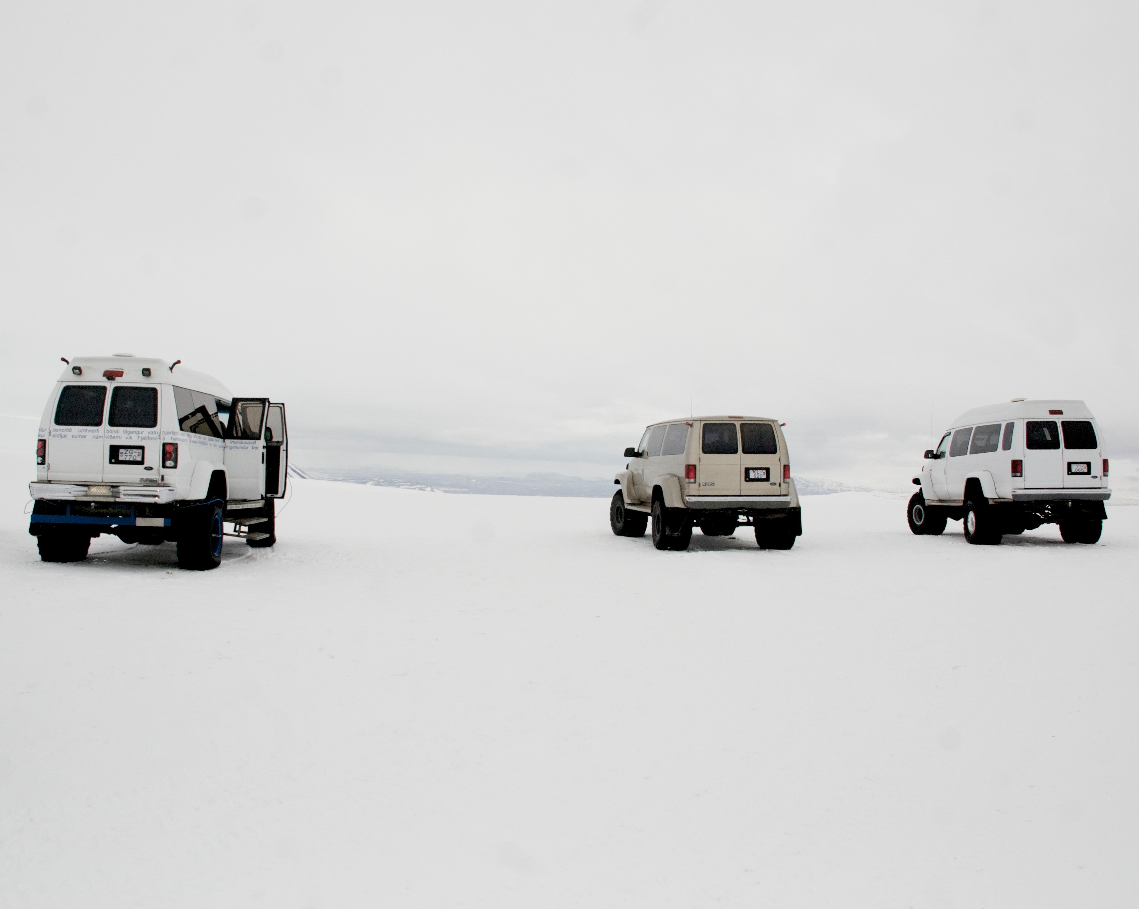 Three four-wheel-drive vehicles cross an open white snowfield.