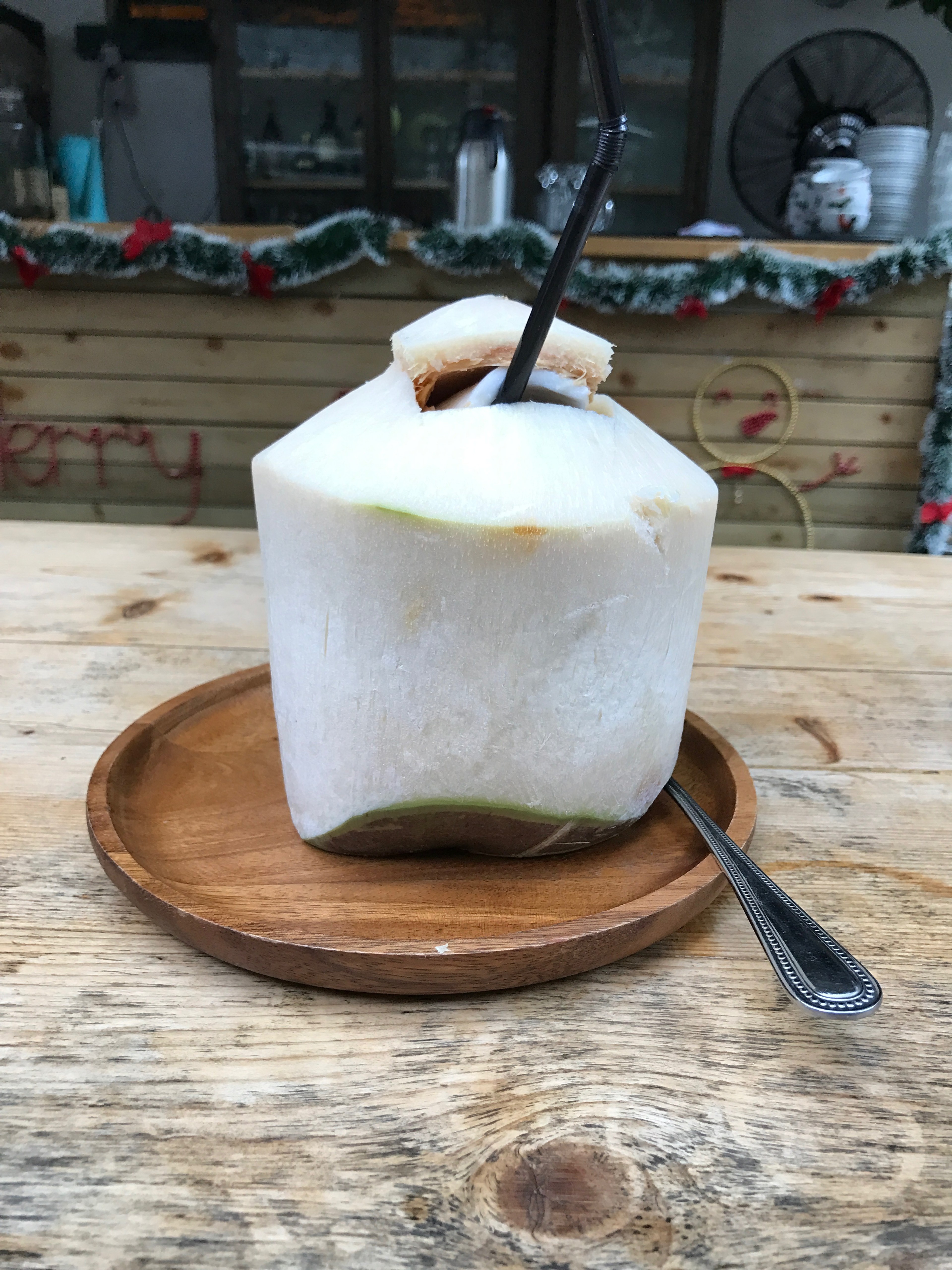 A green coconut drink sits on a wooden board beside a straw.