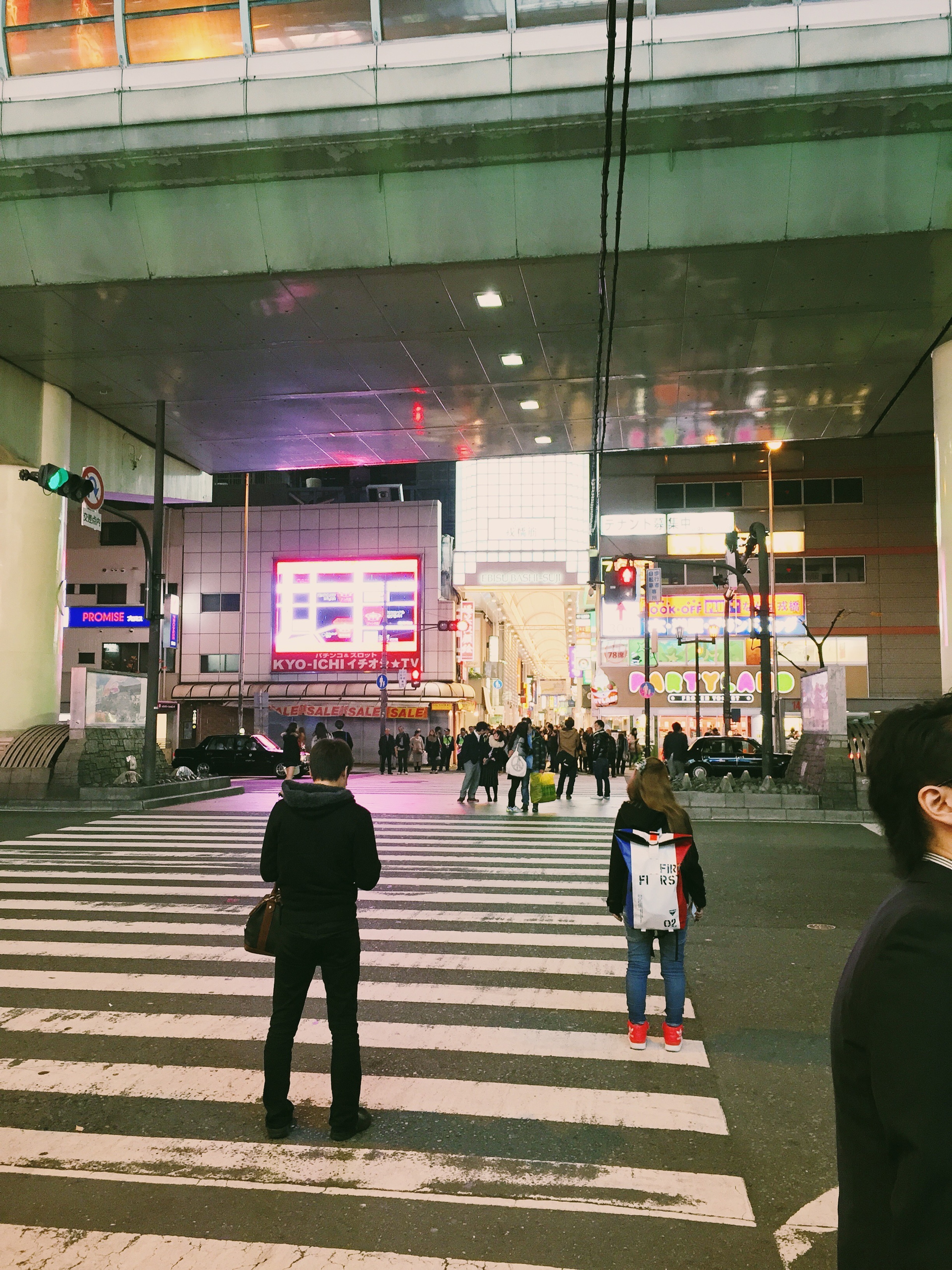 People cross a striped pedestrian walkway toward a modern building entrance.
