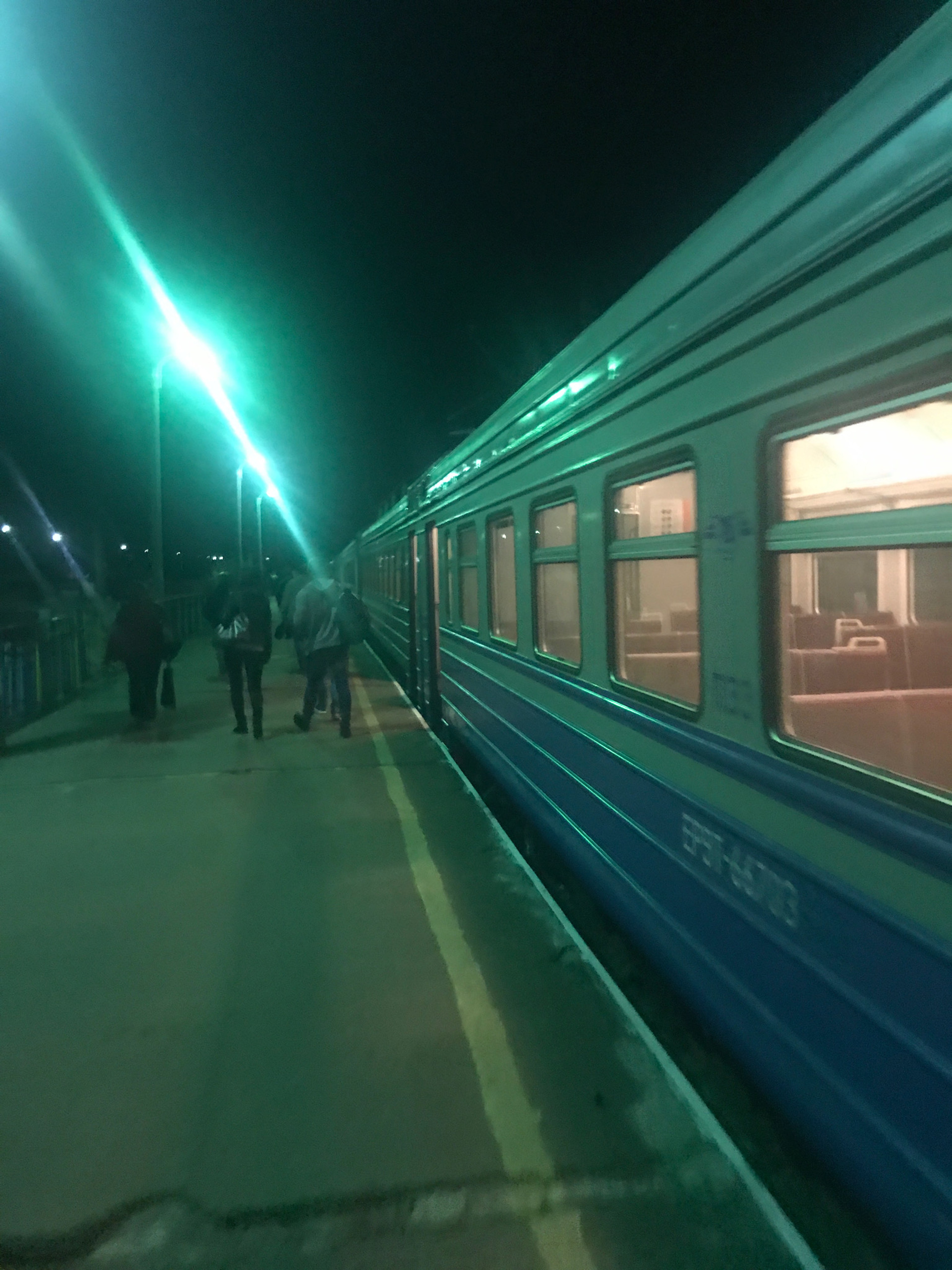 A passenger train stands at a station beneath green lights.