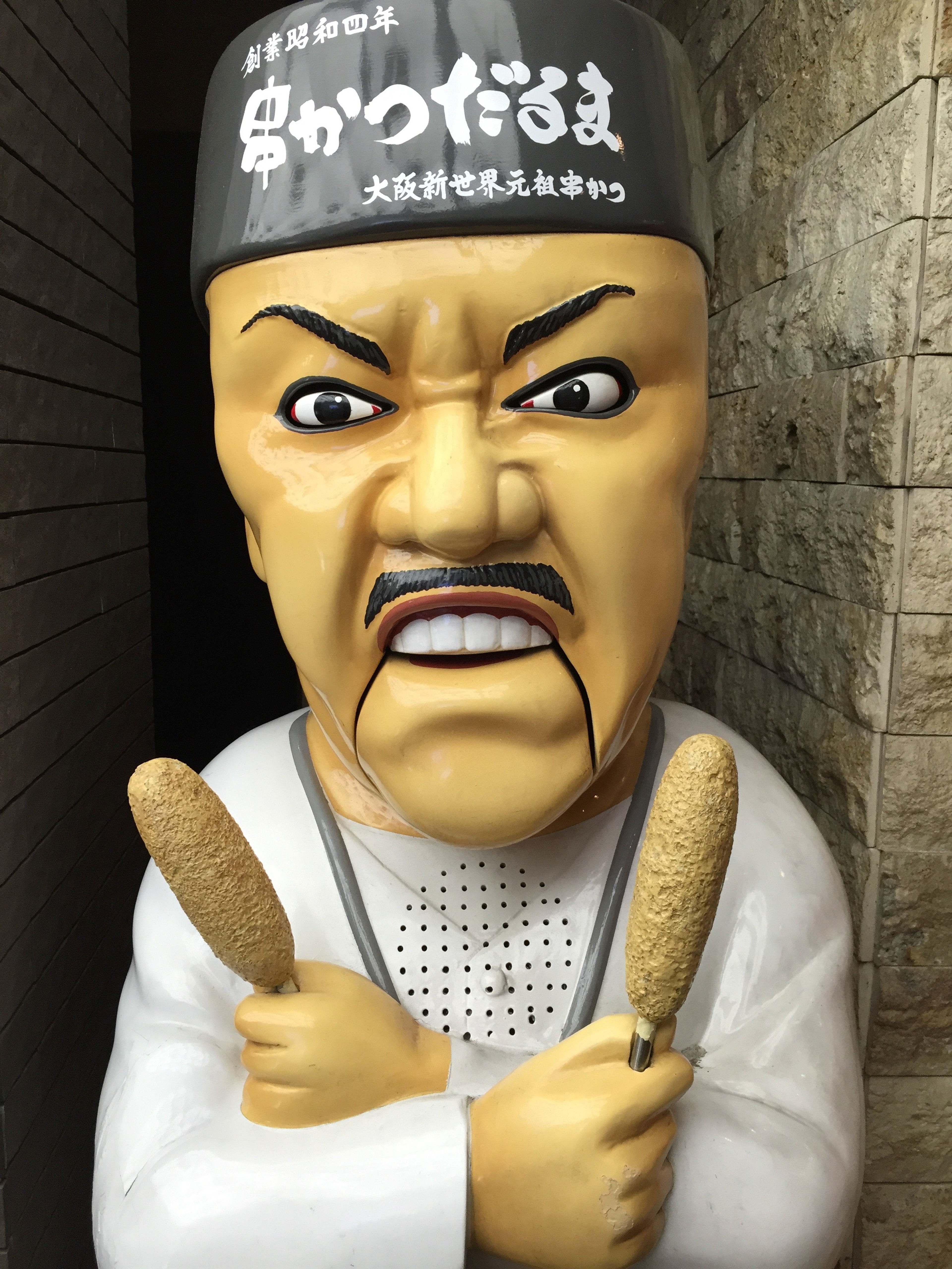 A large cartoon figure stands with crossed arms outside a shop.
