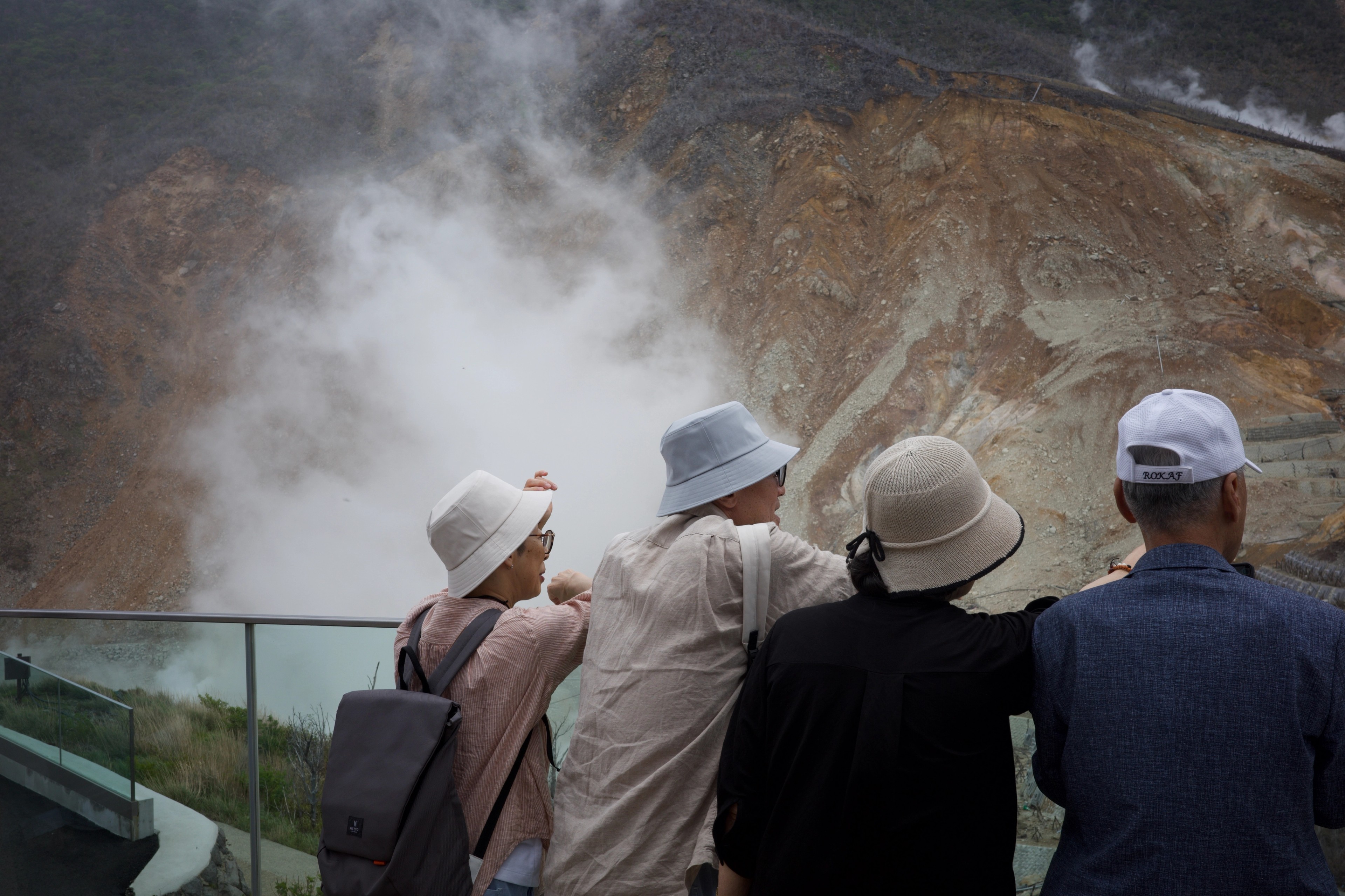Tourists gather at a railing above a steaming geothermal valley.