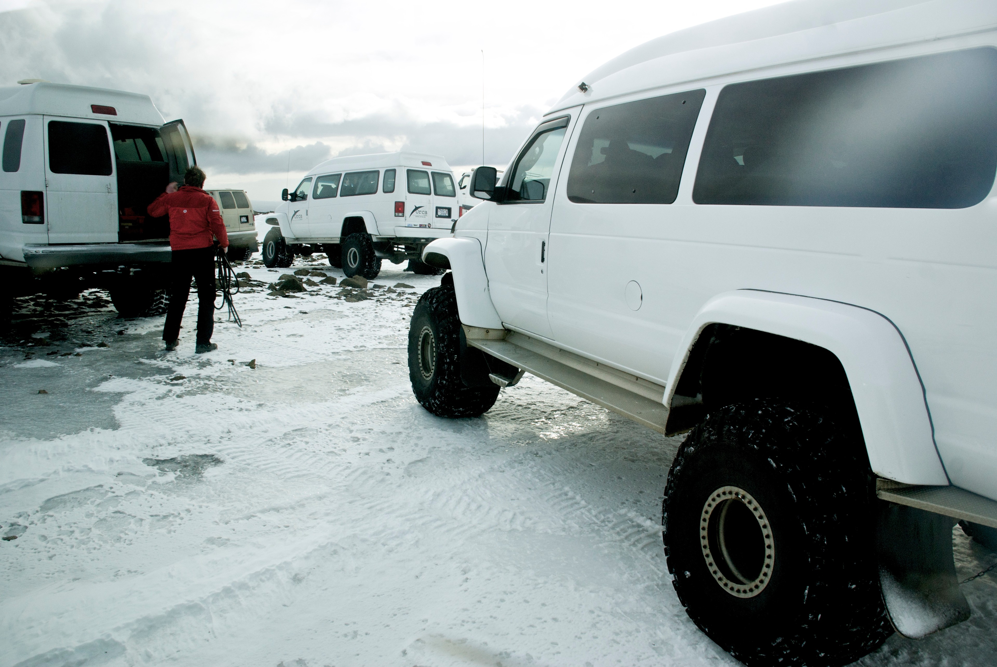 A white vehicle is parked on snow while people stand nearby.