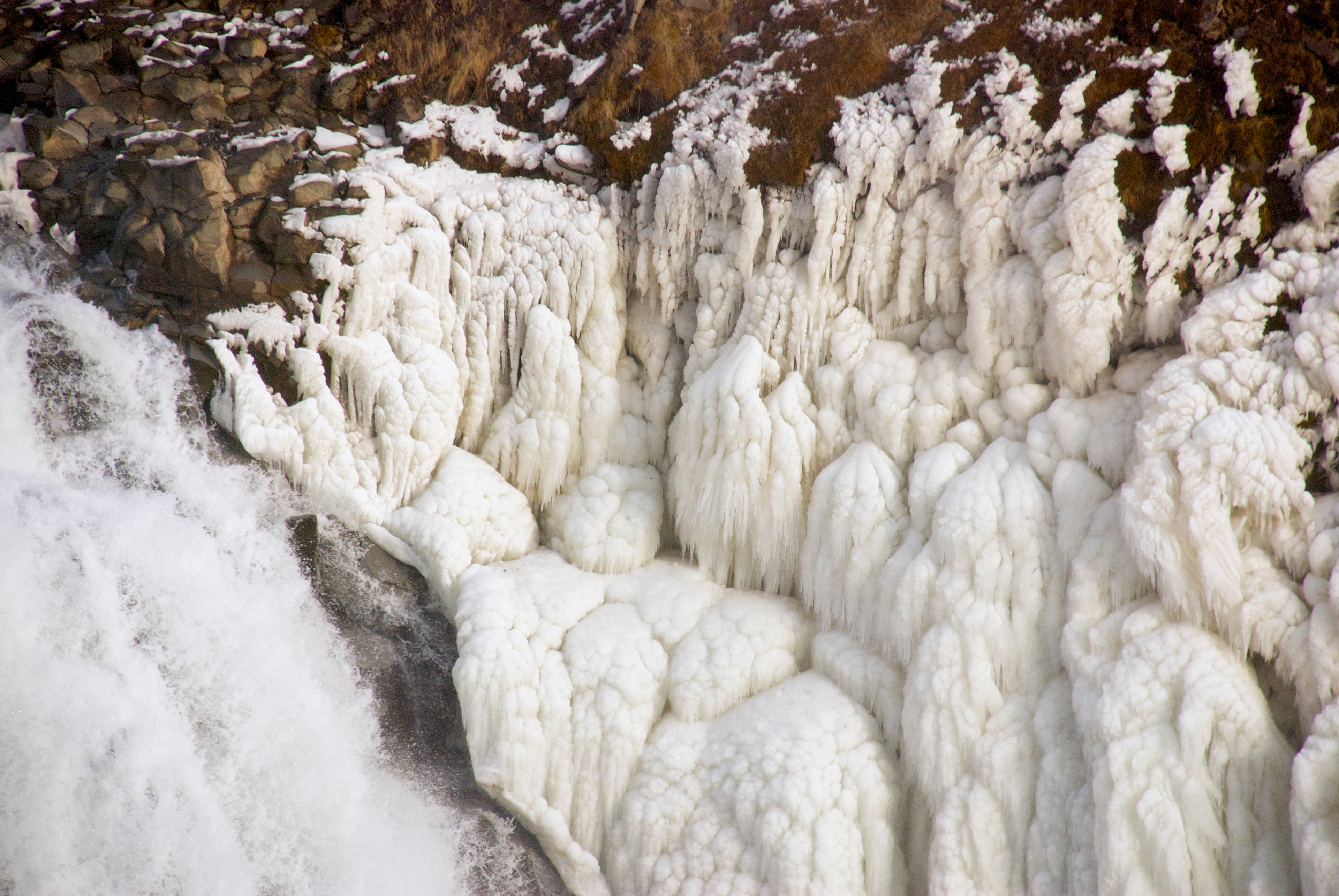 A frozen waterfall hangs in thick white formations above dark rocks.