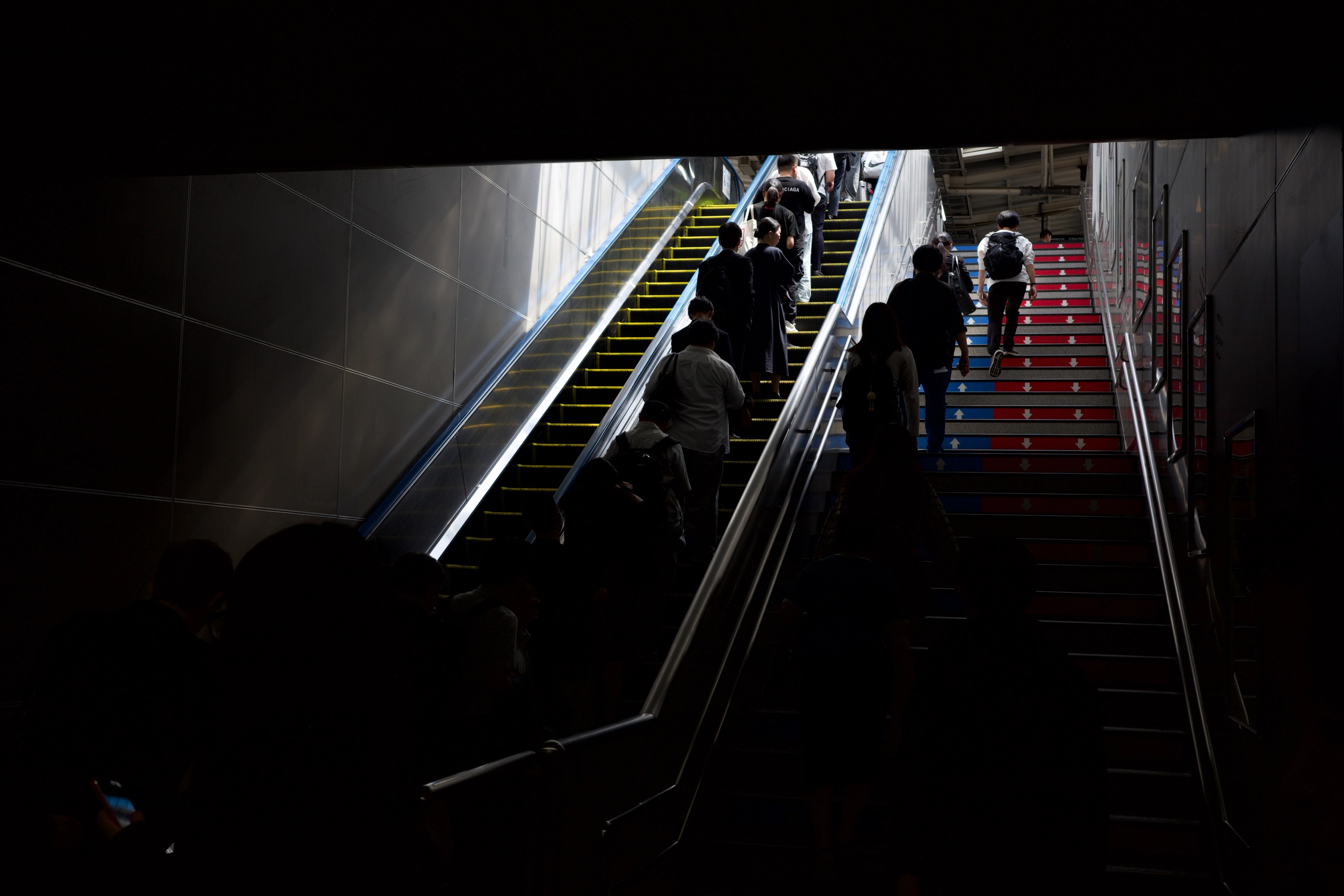 People ride an escalator through a dim subway station.