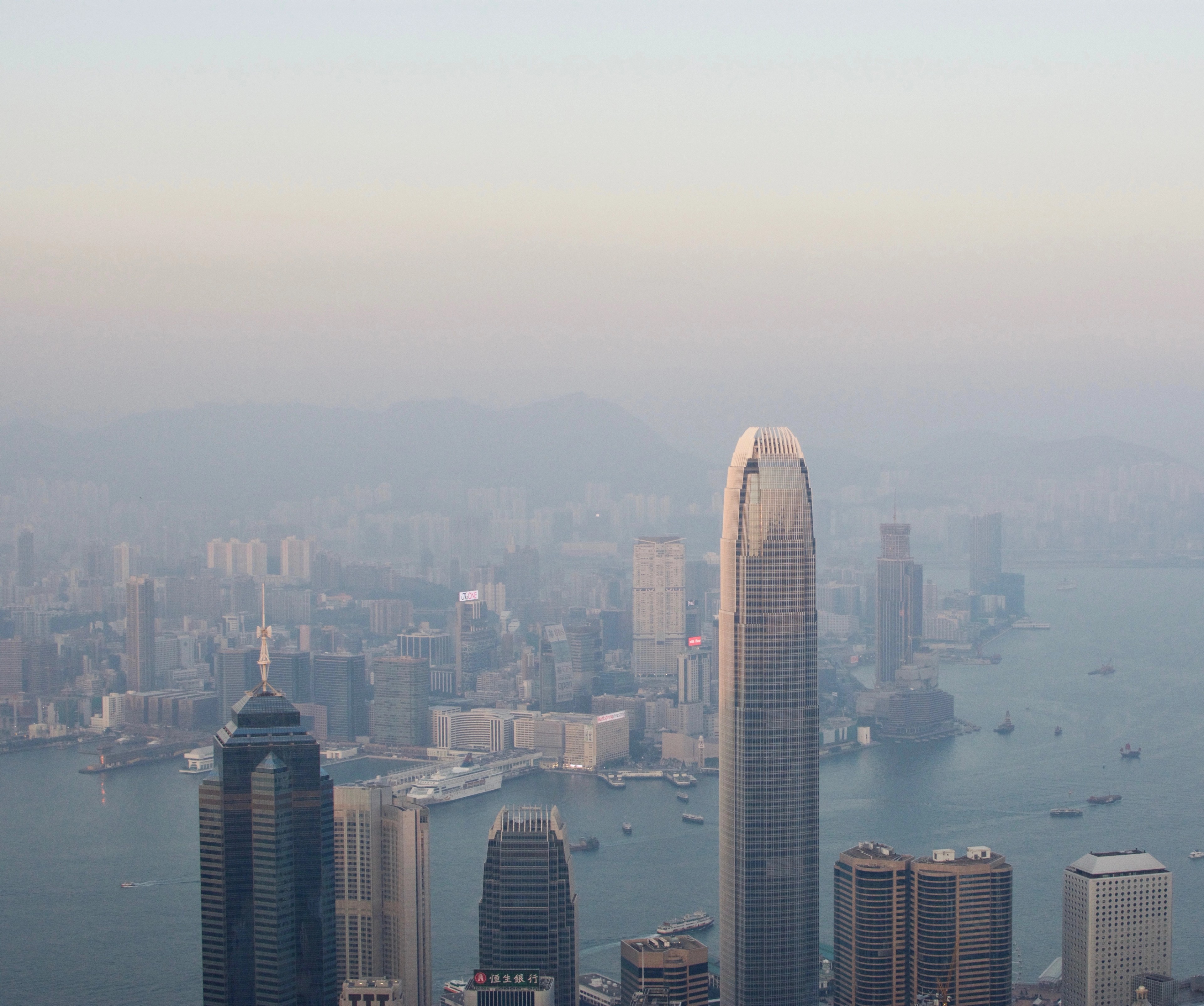 Tall towers rise above a hazy harbor beneath a pale evening sky.