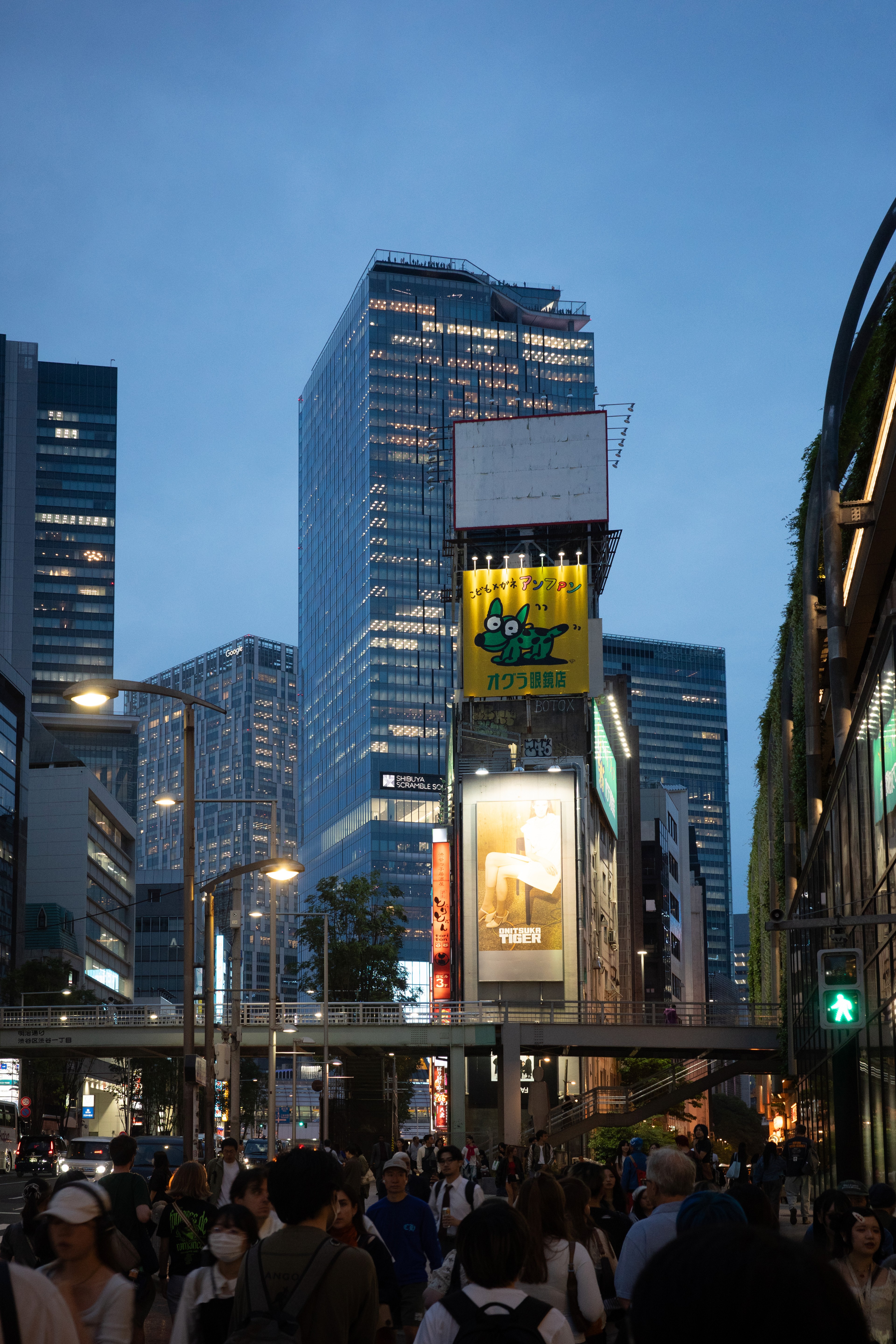 A glass city tower glows at dusk above a crowd.