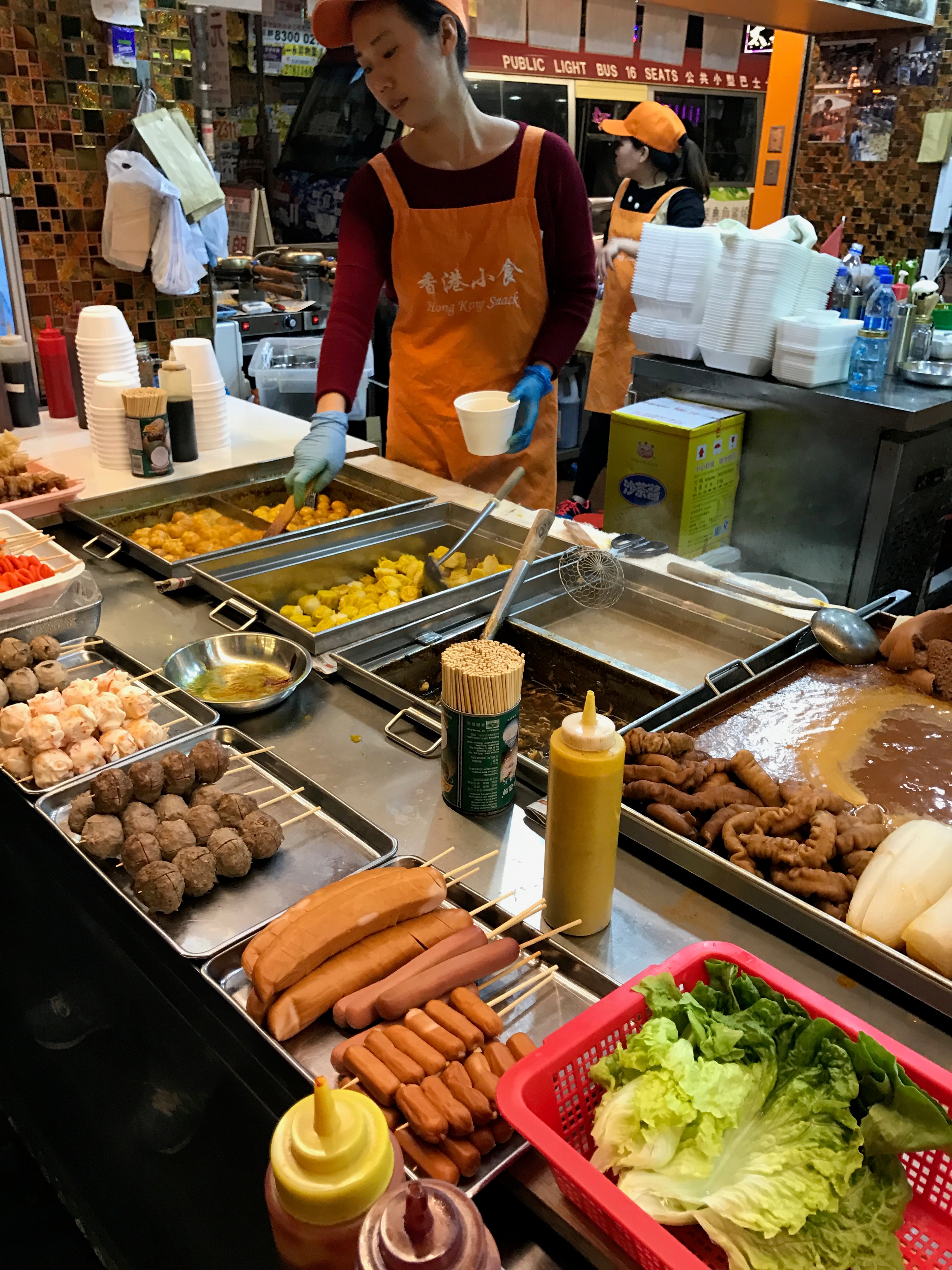 A market counter displays rows of prepared food in metal trays.