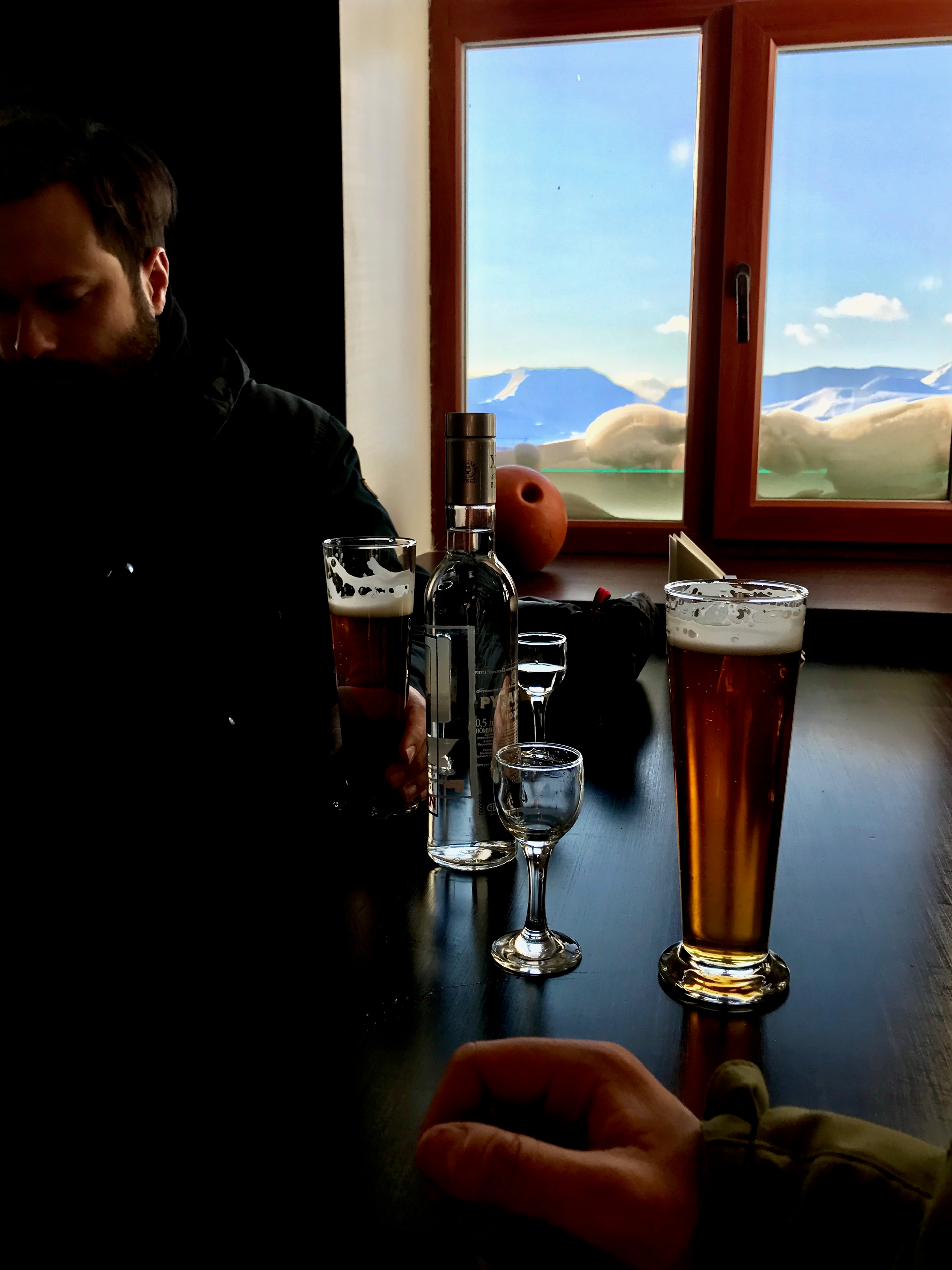 A person pours a drink beside a window looking onto a snowy landscape.