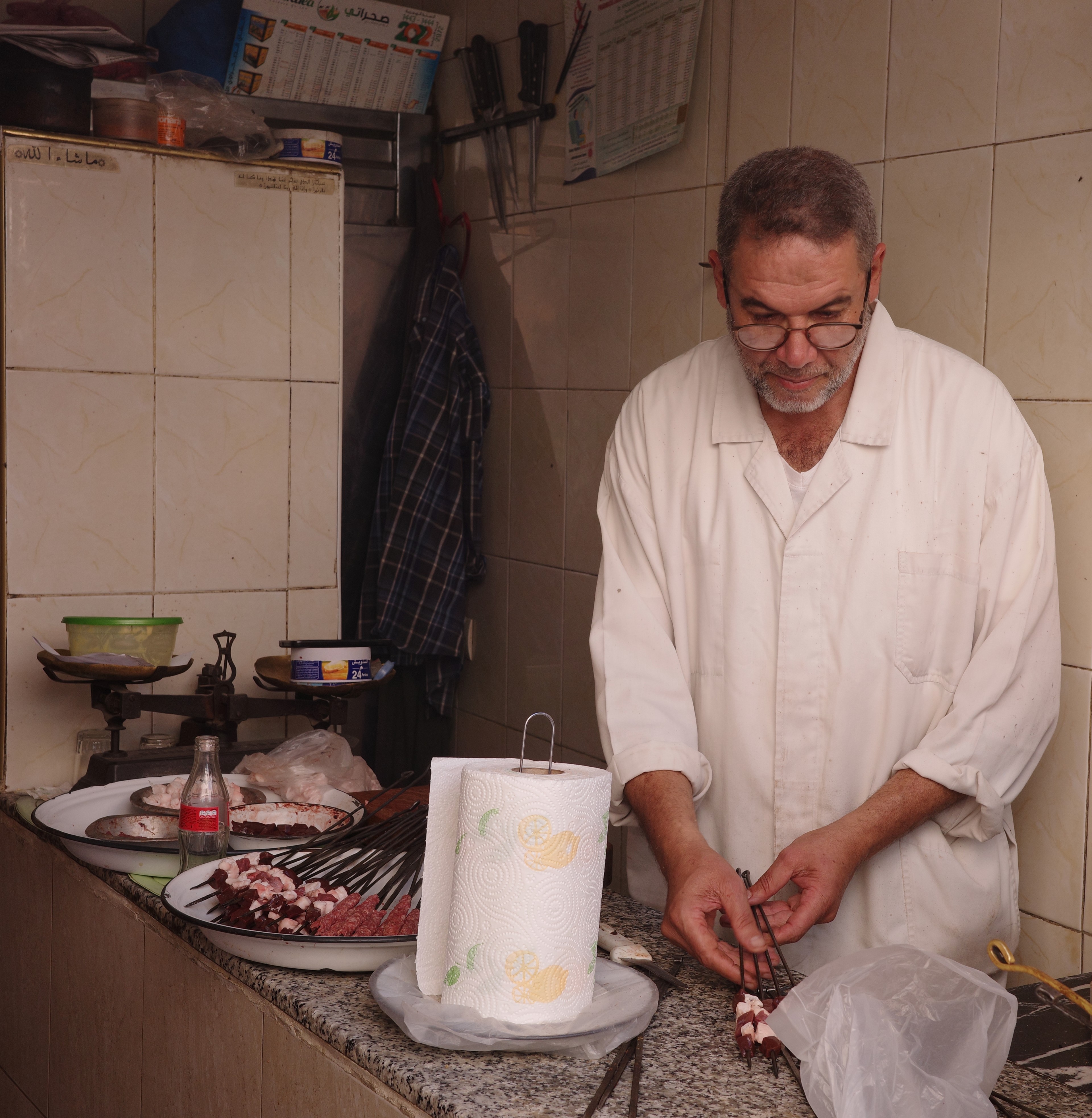 A cook prepares food in a small kitchen beside a tray of ingredients.