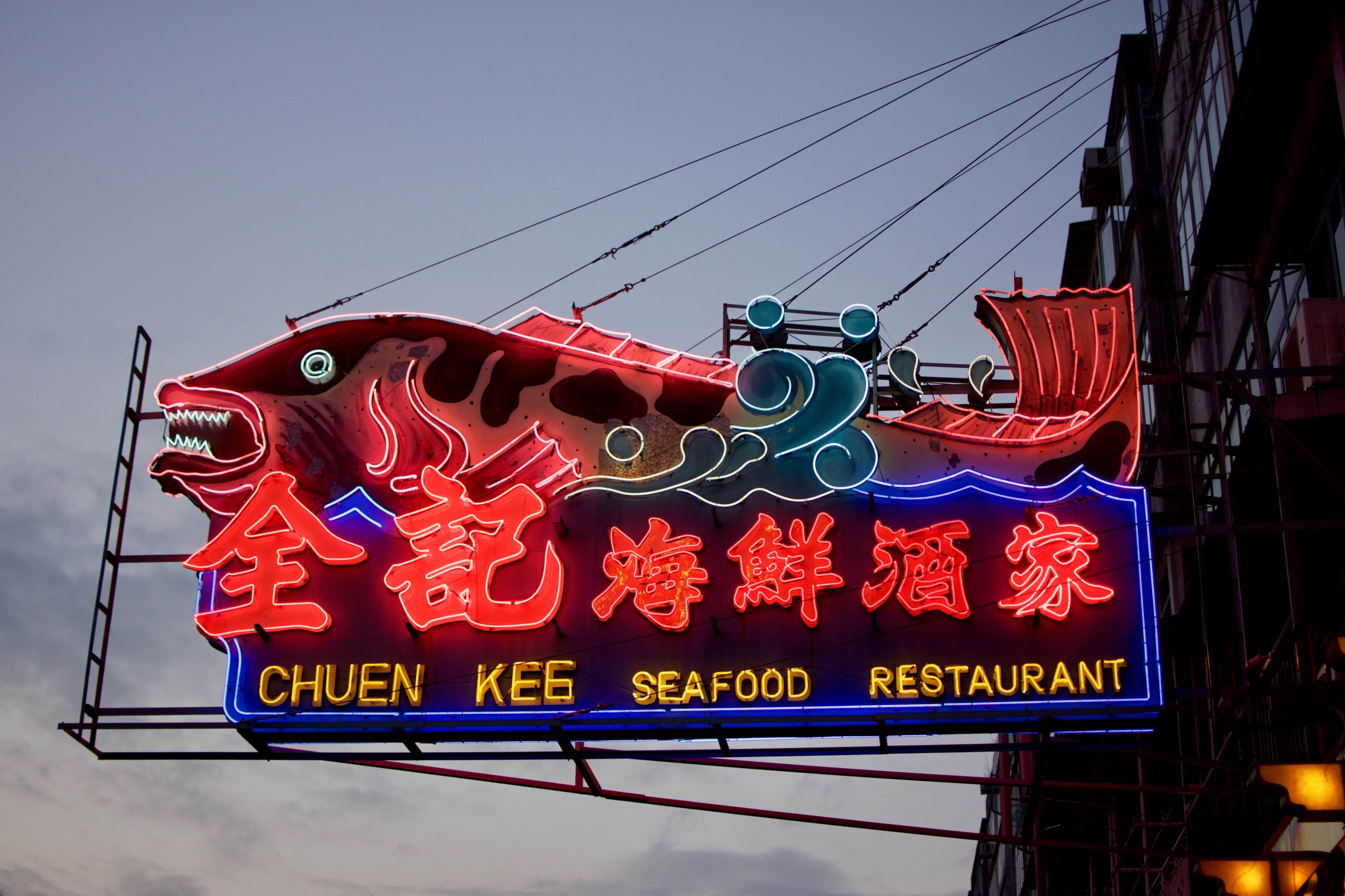A red neon seafood restaurant sign hangs above a Hong Kong street.